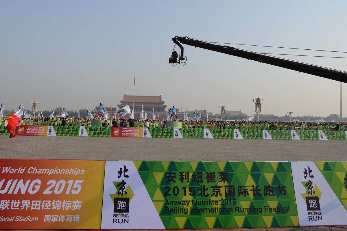 活动举办于天安门广场，现场围挡清晰标注“安利纽崔莱2015北京国际长跑节”“2015国际田联世界田径锦标赛”字样，大批身着绿色服装的参与者集结在场边，旗帜飘扬，现场氛围热烈活力，尽显健康运动的积极风貌。