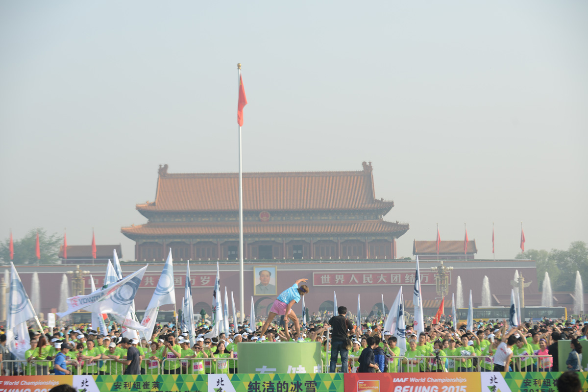 活动在北京天安门广场举办，现场可见“安利纽崔莱”“IAAF World Championships BEIJING 2015”标识，大量身着绿色服装的参与者集结，领操员在台前带领热身，现场旗帜飘扬，氛围热烈活力，充分彰显安利纽崔莱倡导健康运动的品牌理念，参与者热情高涨。