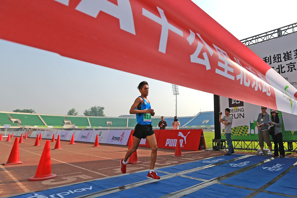 图为安利纽崔莱十公里北京跑（BEIJING RUN）赛事现场，参赛选手正冲刺抵达终点，跑道旁设置醒目的安利品牌标识，现场工作人员持设备记录赛事瞬间，氛围热烈昂扬，彰显安利倡导健康运动的品牌理念。