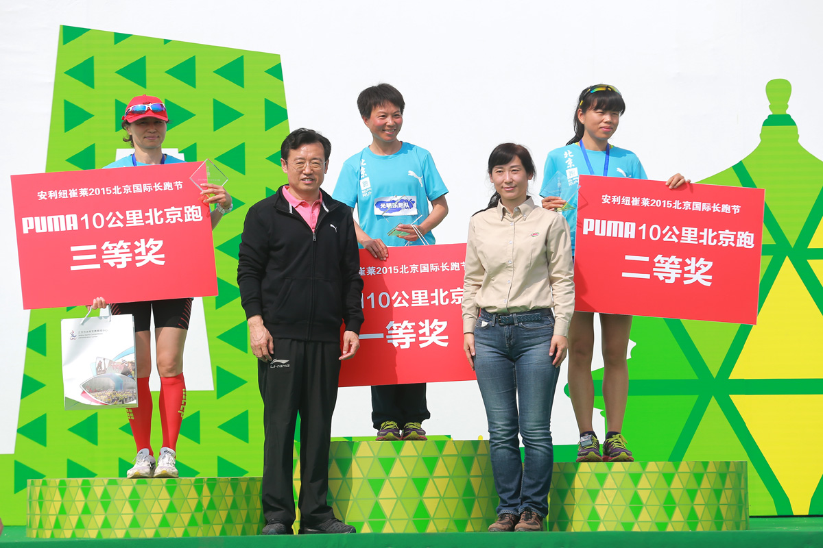 图为安利纽崔莱2015北京国际长跑节PUMA10公里北京跑颁奖现场，三名获奖选手立于领奖台，分别手持对应一二三等奖的标识牌，两位颁奖嘉宾站在领奖台前，现场氛围昂扬热烈，传递出安利倡导健康运动的正向品牌理念。