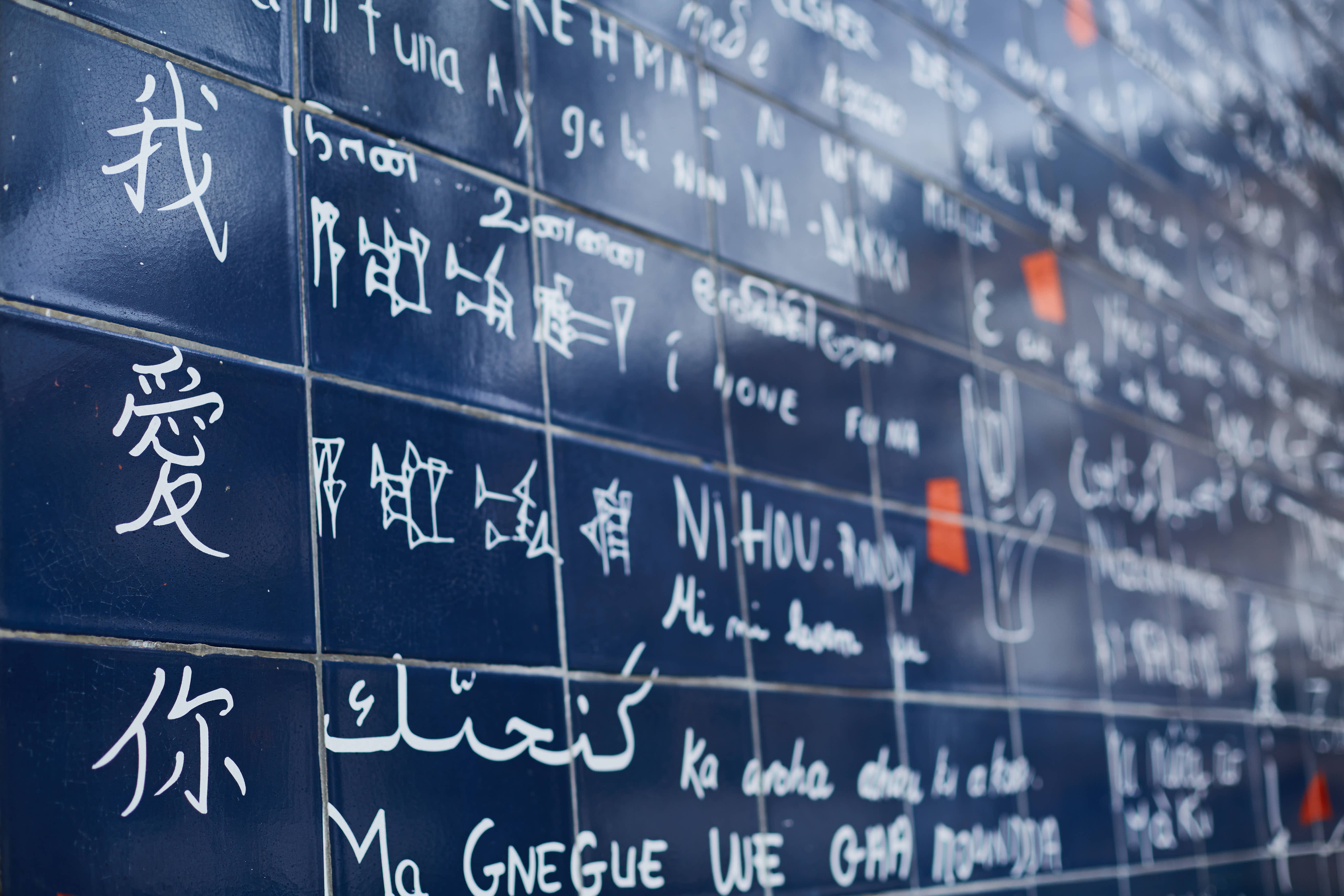 深蓝色瓷砖墙面上，用手写字体呈现了数百种不同语言的“我爱你”表述，画面左侧醒目的中文手写“我、爱、你”尤为亮眼，整体氛围温暖包容，传递跨越地域与语言的美好爱意，彰显安利传递温暖、联结大众的品牌温度。