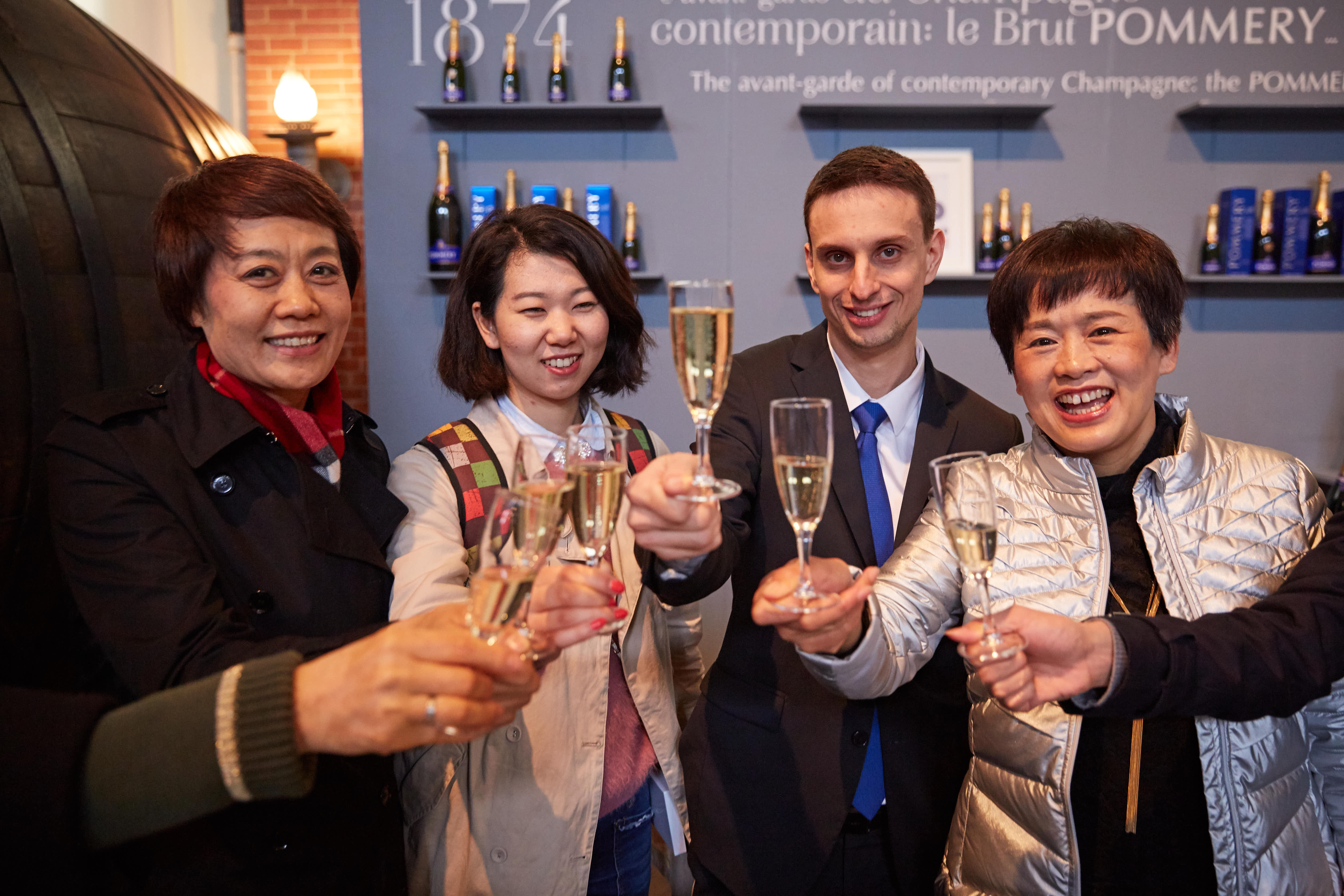 活动现场背景为POMMERY香槟展示区，几位安利伙伴与外籍友人面带灿烂笑容，共同举起盛有香槟的高脚杯碰杯致意，现场氛围热烈融洽，尽显伙伴共聚的喜悦与活动的欢庆氛围。