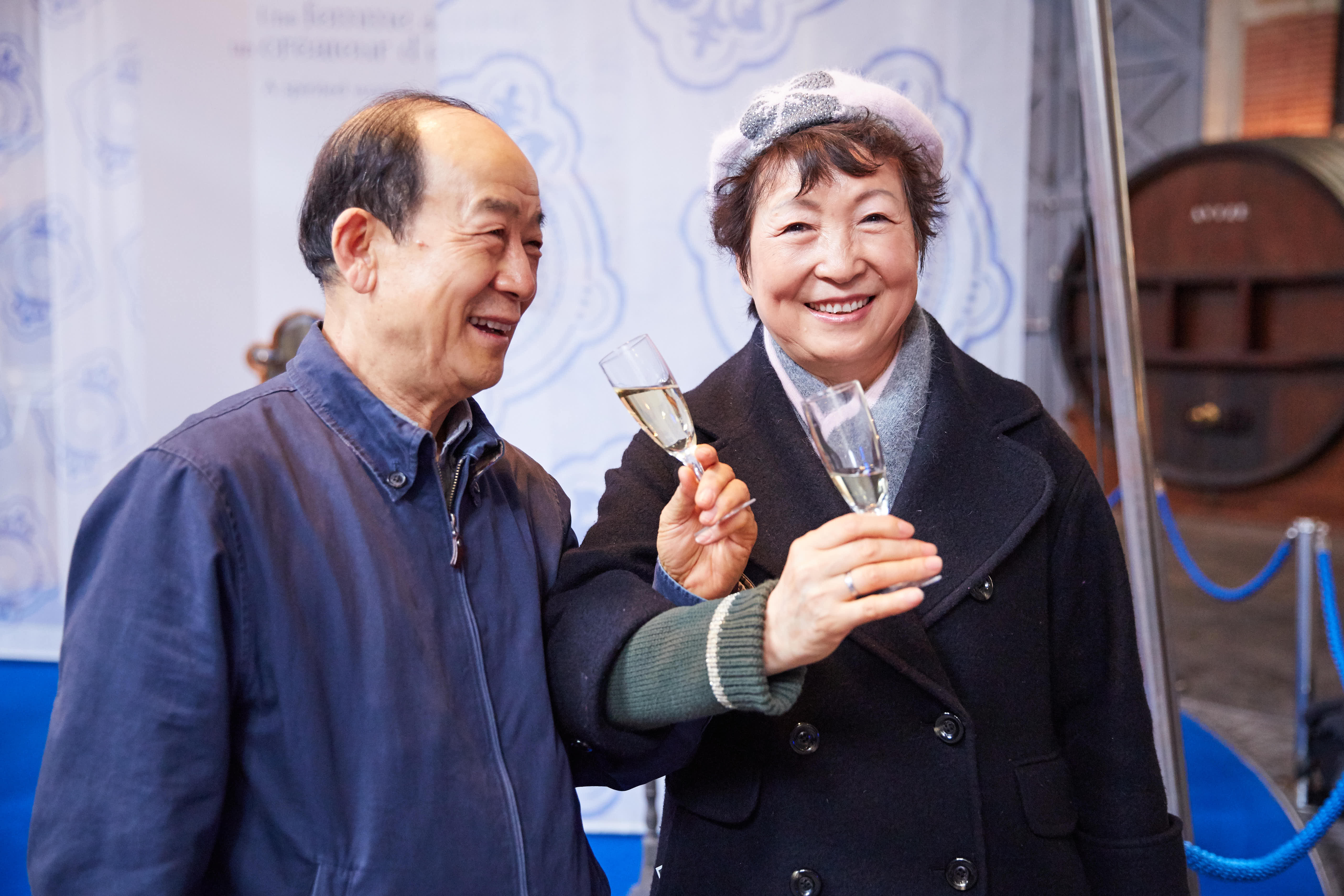 安利品牌线下活动现场，两位资深合作伙伴满面和煦笑容，共同举起盛有饮品的高脚杯致意，现场氛围轻松愉悦，尽显伙伴们参与活动的满满获得感与喜悦心情，传递出安利温暖正向的品牌氛围。