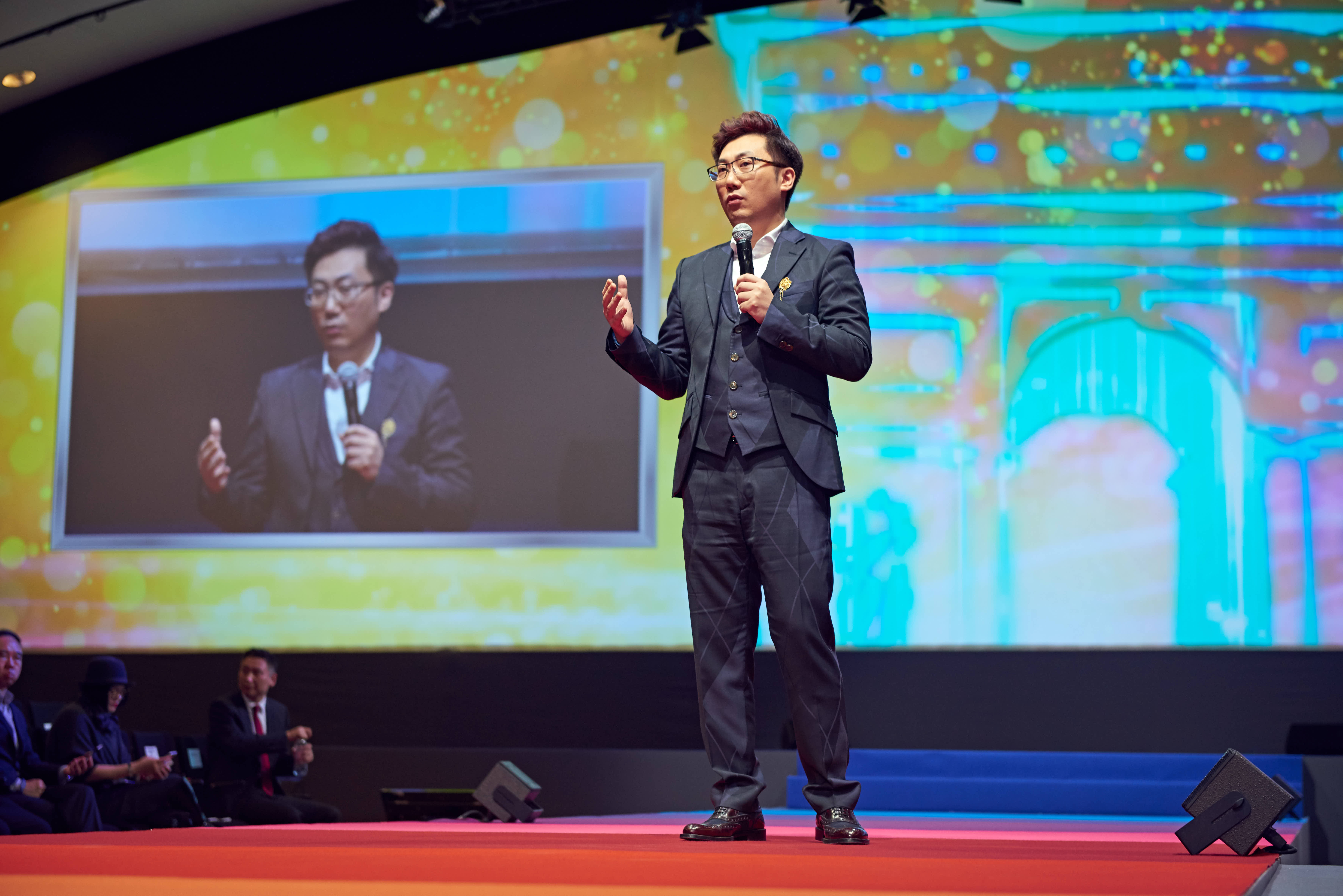 本次安利品牌活动现场，身着正装的精英嘉宾手持麦克风站在舞台上分享发展心得，身后大屏同步直播其演讲画面，台下参会人员认真聆听，现场氛围专业热烈，充分彰显安利伙伴奋进向上的良好风貌。