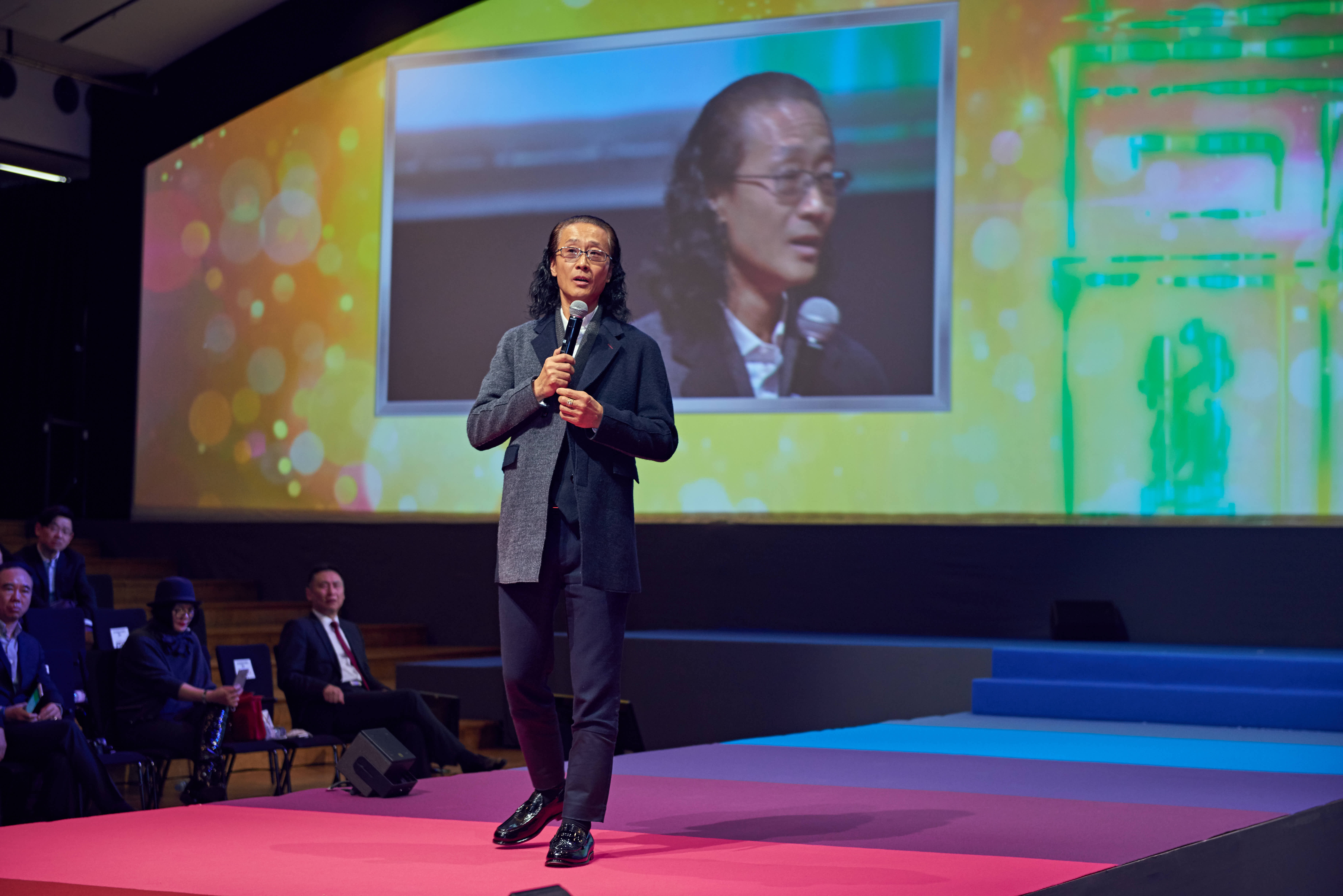 本次安利研讨会活动现场，特邀嘉宾手持麦克风站在舞台上做内容分享，身后大屏同步实时展示嘉宾的分享画面，台下参会的伙伴认真聆听，现场氛围专业热烈，尽显安利活动积极向上、共促成长的良好风貌。