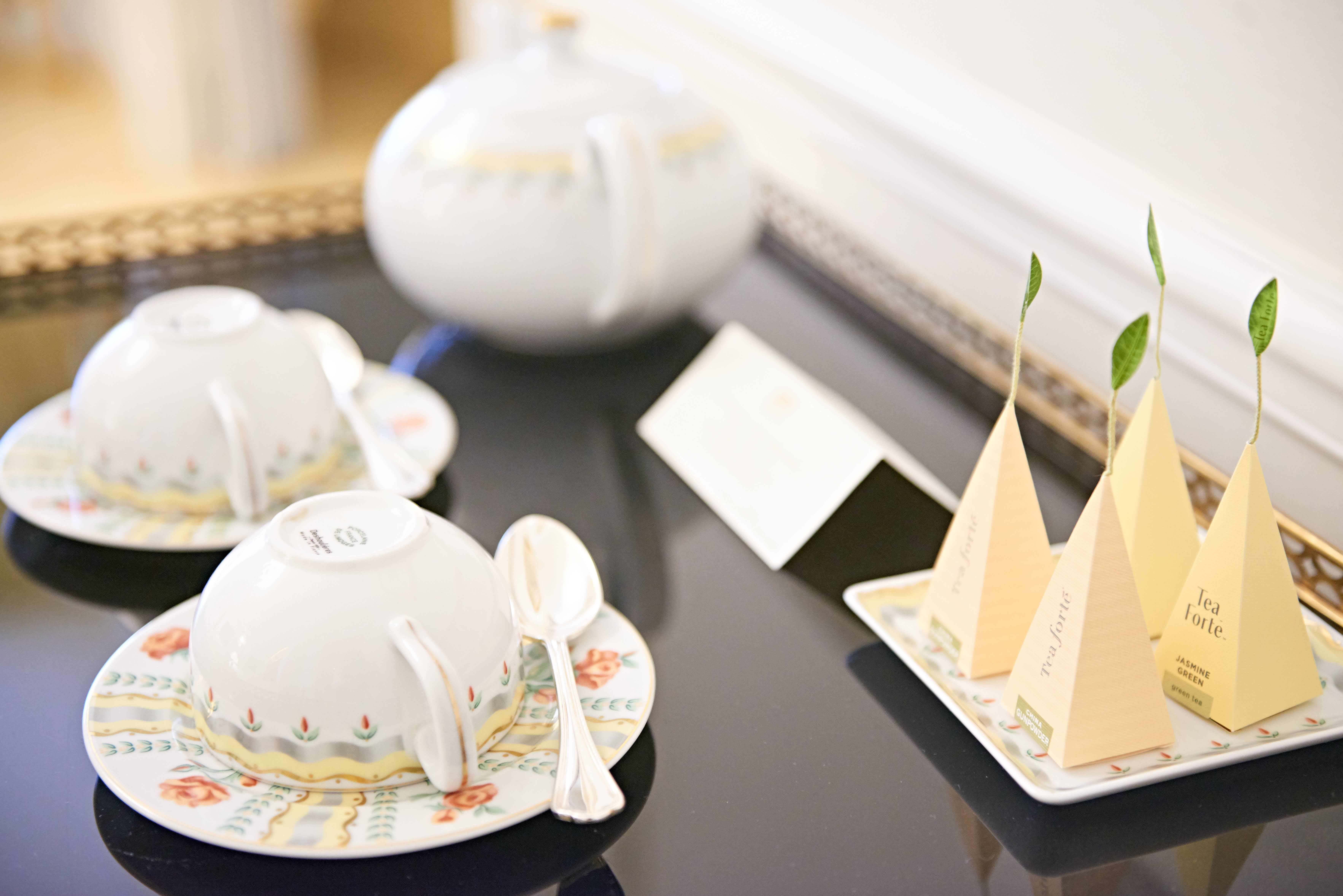 画面摆放着印花精美的瓷质茶具，一旁托盘陈列着Tea Forte品牌金字塔造型茶包，包含茉莉绿茶等多款茶品，整体布置雅致温馨，尽显安利品牌活动的细腻用心，为参会人员营造舒适贴心的休憩体验。
