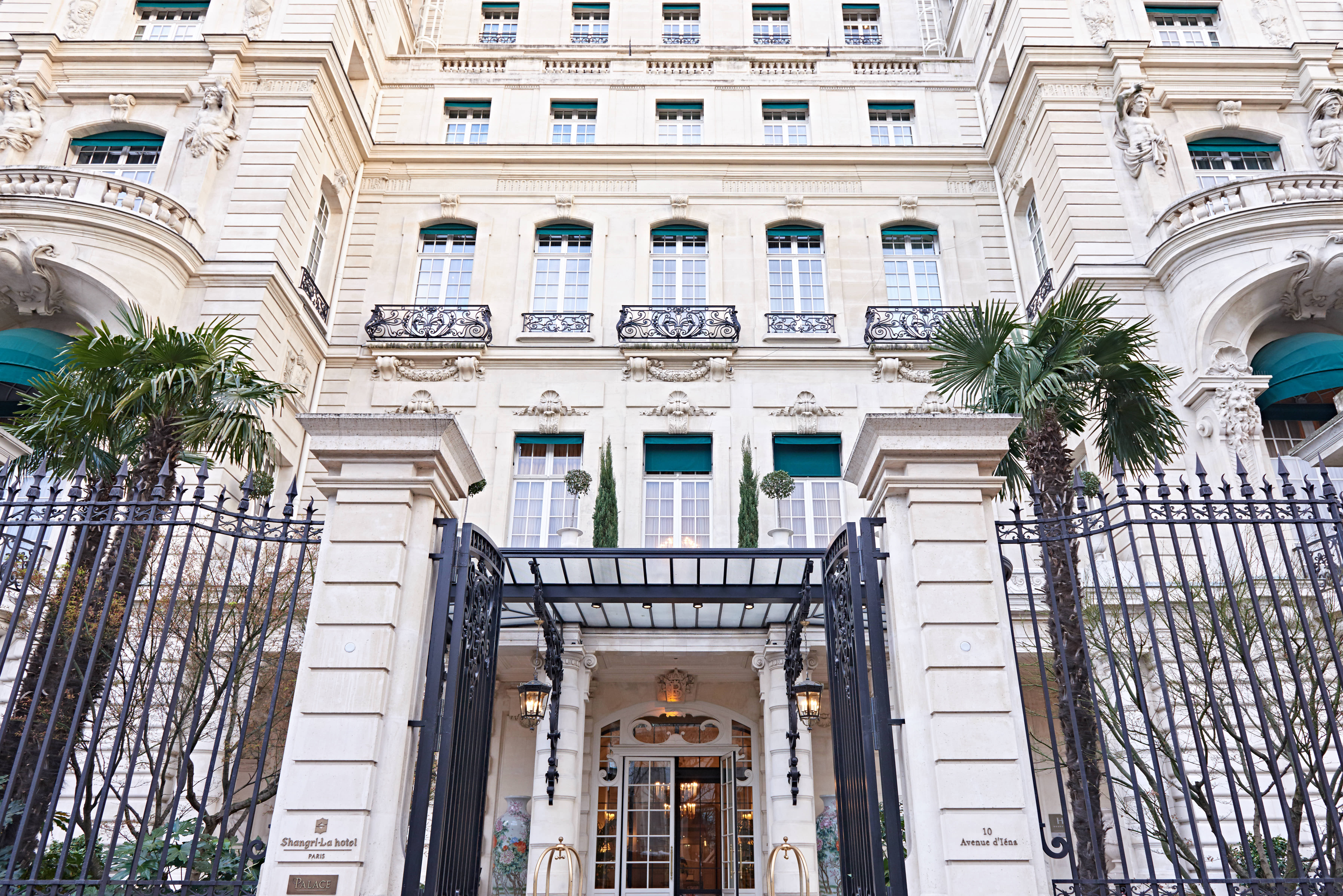 本次安利海外活动选址巴黎香格里拉酒店（Shangri-La hotel PARIS），酒店坐落于10 Avenue d'Iéna，属Palace级高端场地。画面展现酒店典雅法式建筑外观，雕花铁艺大门庄重精致，绿植点缀其间，整体氛围恢弘华贵，尽显活动高端定位。