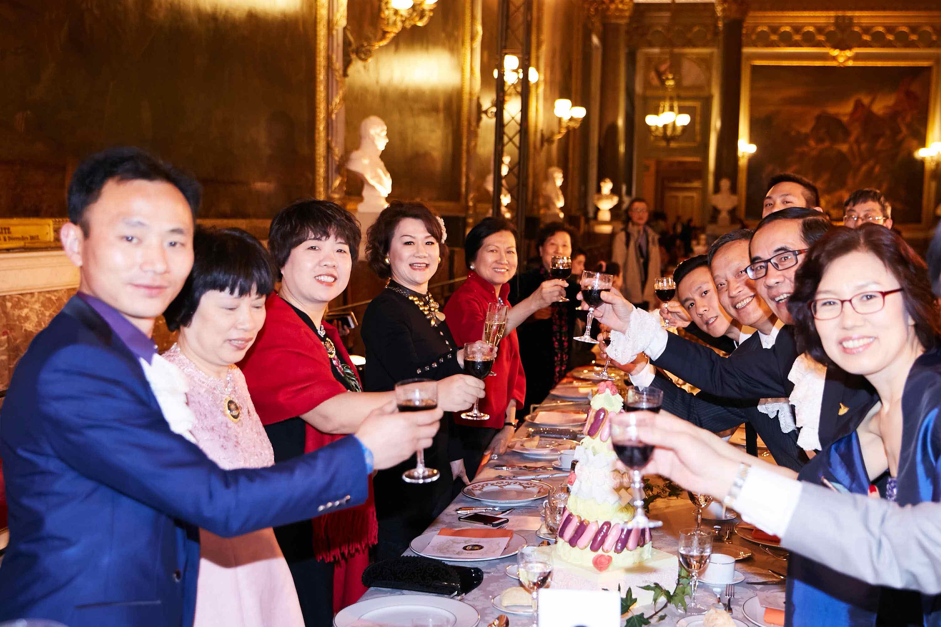 在典雅奢华的欧式宴会厅内，多位安利核心伙伴齐聚长餐桌旁，大家面带灿烂笑容共同举杯致意，桌间摆放着精致餐点与装饰精美的庆祝蛋糕，现场氛围热烈融洽，尽显伙伴们共贺佳绩、聚力同行的昂扬风貌。