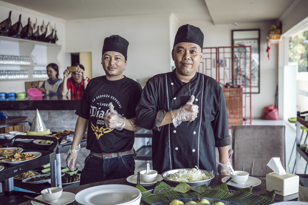 安利活动餐饮服务区内，两位餐饮工作人员佩戴工作帽与一次性食品手套，站在摆放着新鲜食材、餐具与餐食的桌前共同竖起大拇指，神态自信从容，彰显出对本次活动餐食服务品质的充足信心，现场氛围热忱贴心，为参会伙伴提供优质餐饮保障。