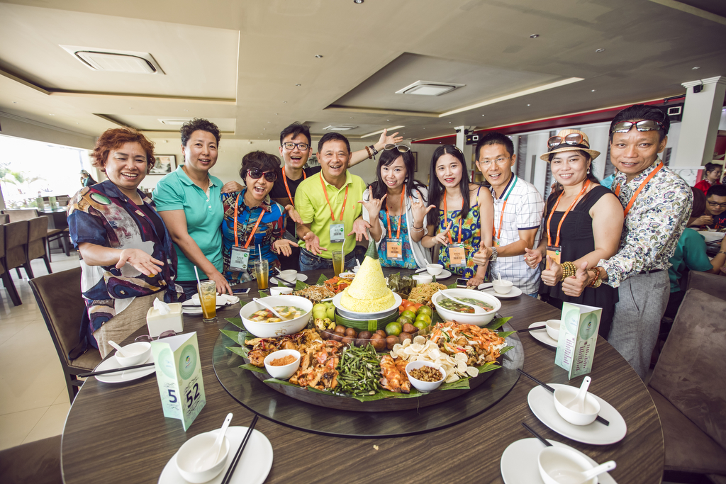 佩戴参会证件的安利伙伴们围在标有“5 52”的餐桌旁，桌上摆满丰盛特色佳肴，众人面带灿烂笑容，有的比出活泼手势、有的竖起拇指，氛围热烈欢快，尽显团队融洽的凝聚力与活动的愉悦氛围。