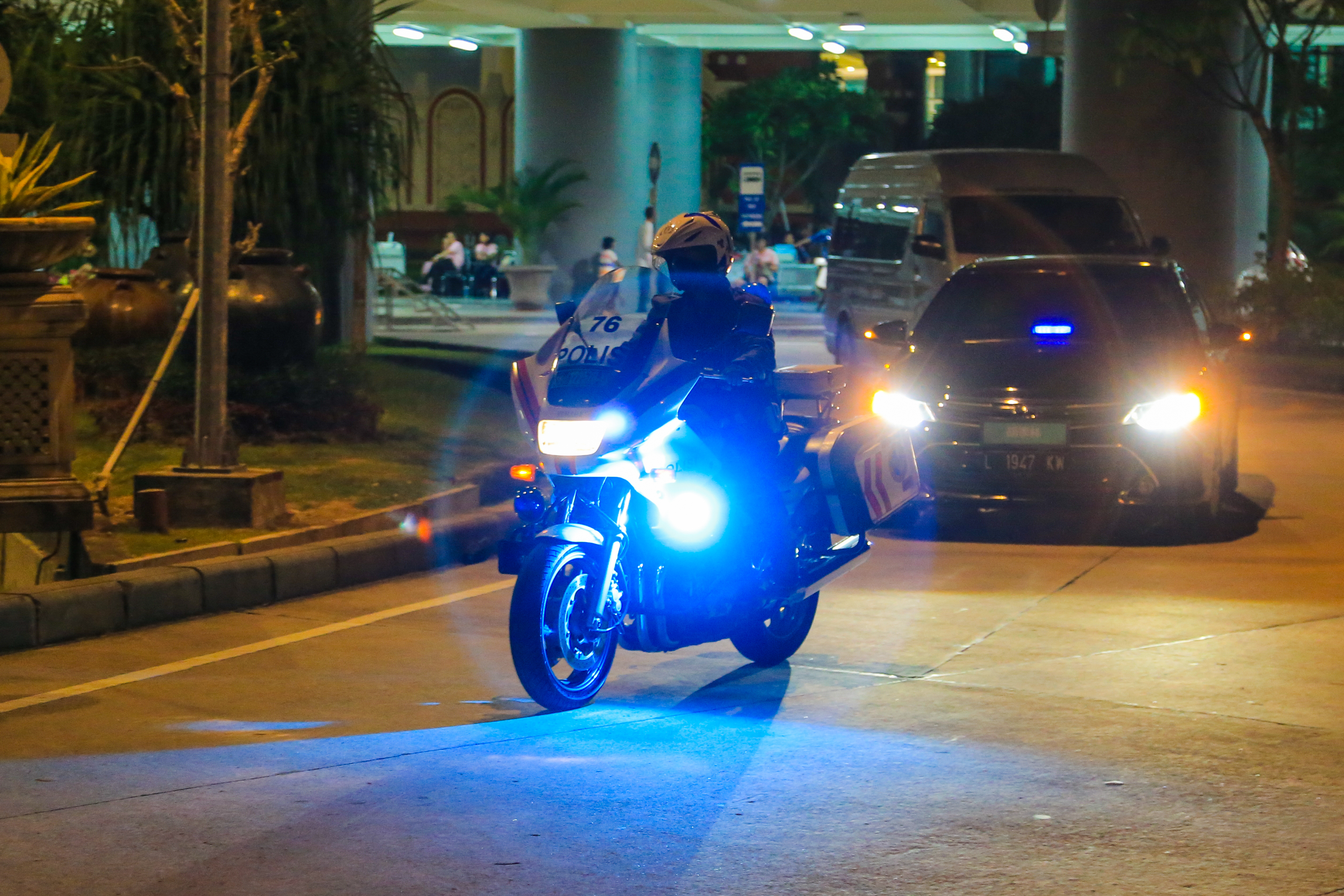 夜幕下，印有“76 POLIS”的警用摩托亮着蓝白警示灯在前开道，后方跟随亮灯的护航车辆，周边可见道路绿化、建筑立柱与等候人员，现场秩序井然，为安利活动参与人员出行提供安全保障，尽显活动高规格与周到安排。
