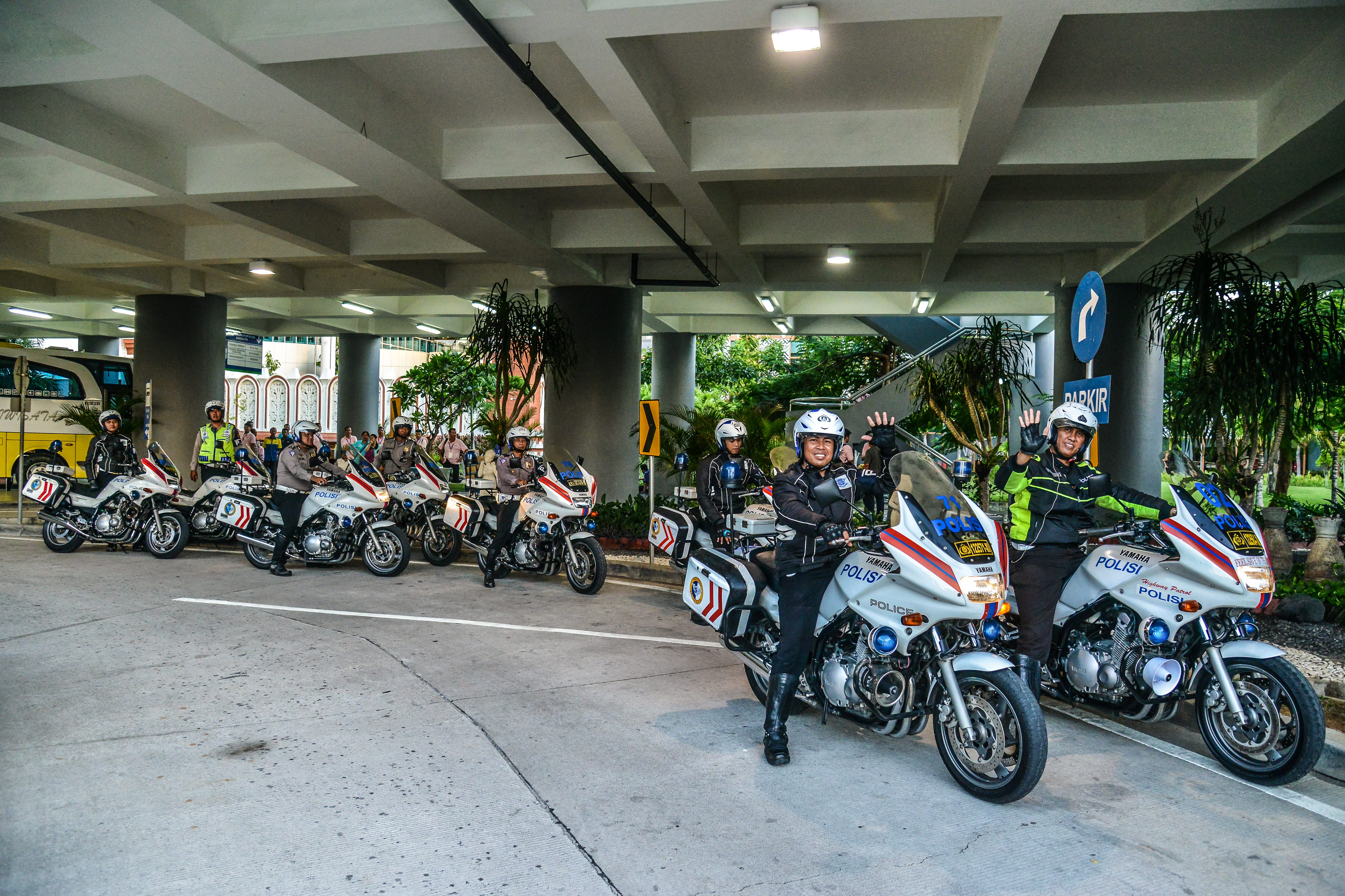 数名身着专业制服的警员驾乘印有“POLISI”标识的警用摩托，在标注“PARKIR”的停车区域整齐列队，警员们精神饱满，前排警员友好挥手示意，全员整装待发，为本次安利品牌活动提供出行安全保障，全力护航活动顺利开展。