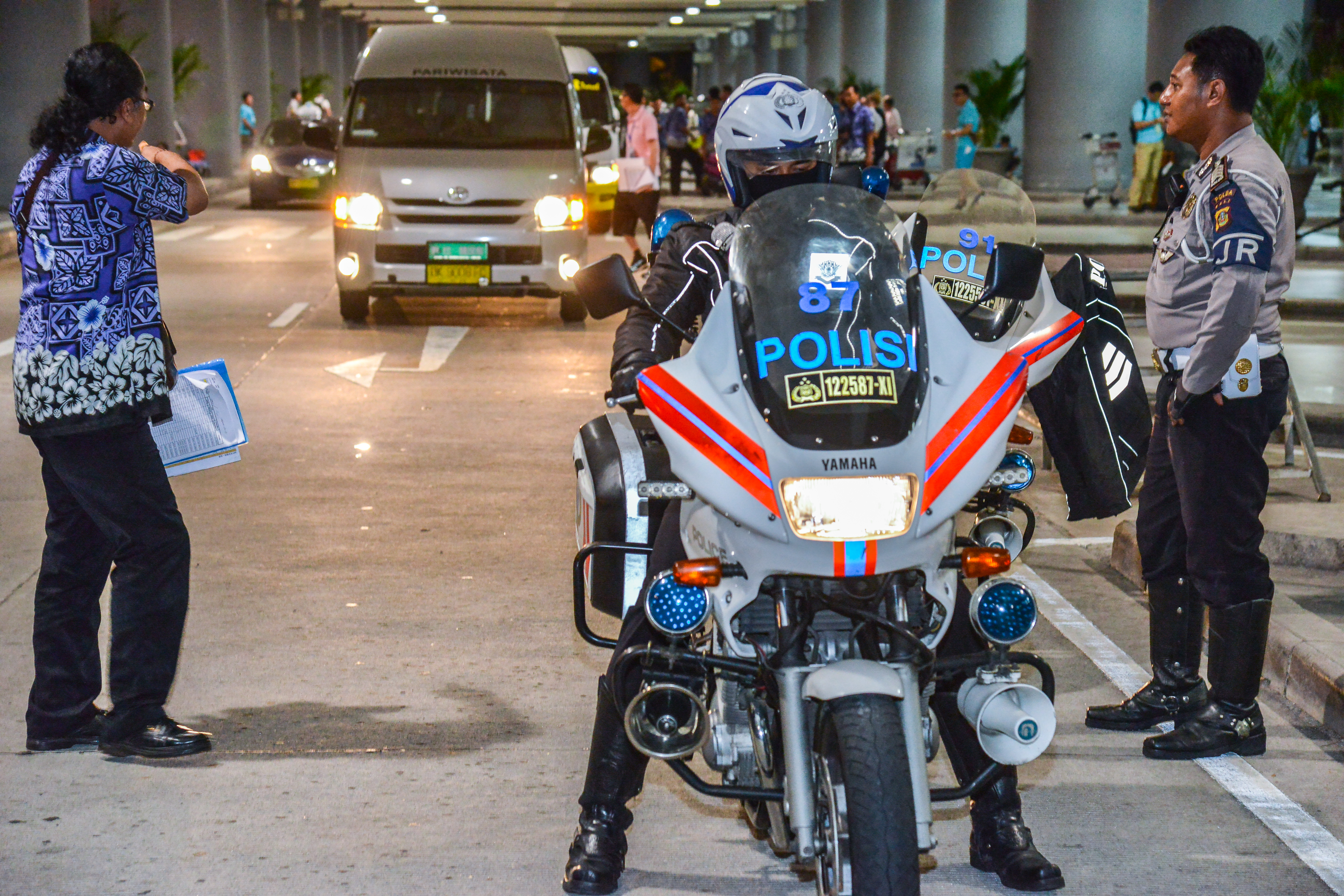 现场印有“POLISI”标识的警用摩托旁，警务人员值守就位，后方接驳车辆有序等候，工作人员在旁协调相关事宜，整体秩序井然，全力为安利海外活动参会人员的出行安全保驾护航，保障活动行程顺畅有序。