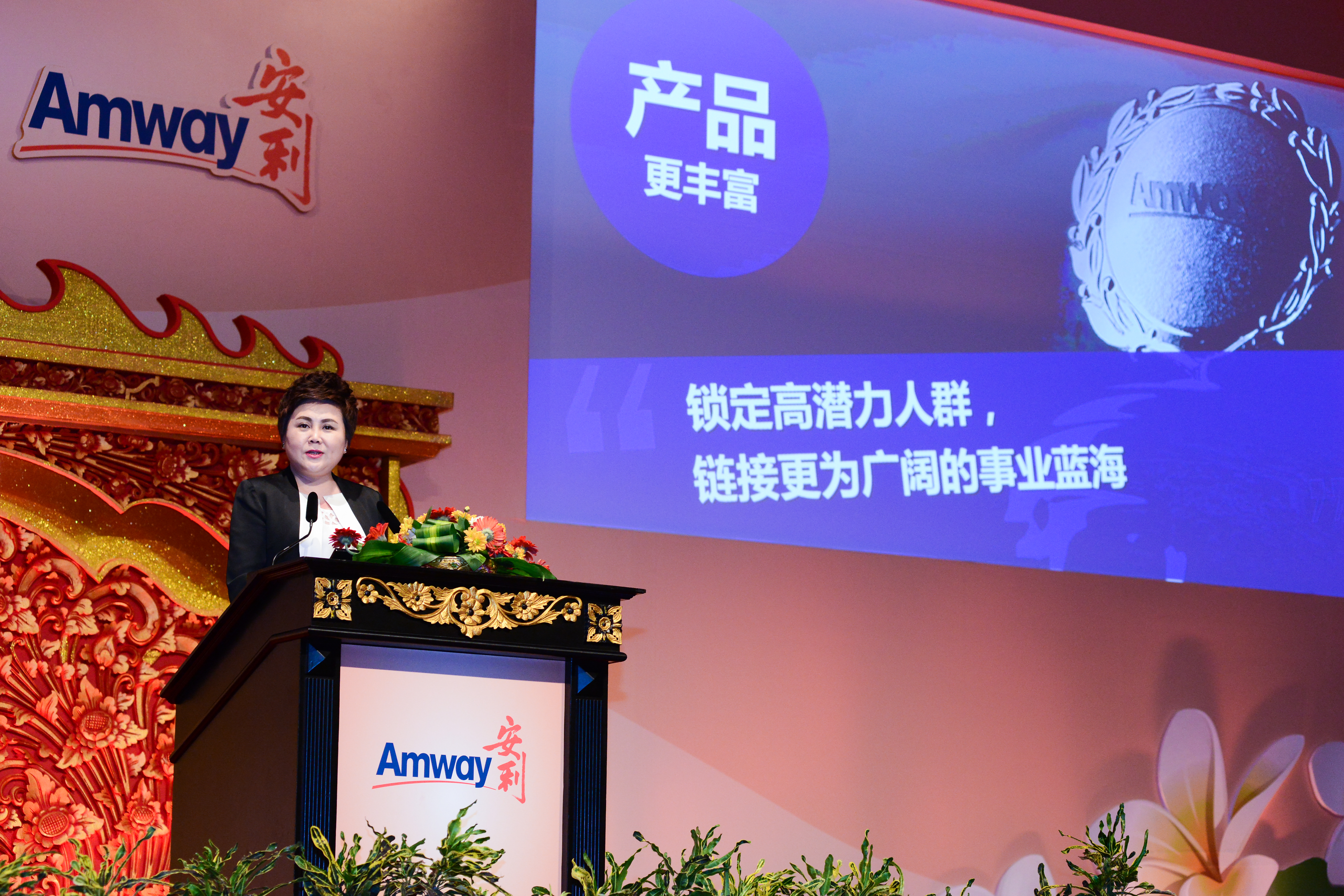 本次安利品牌会议现场，女性嘉宾正立于印有Amway安利标识的精美演讲台发言，背景大屏显示“产品更丰富”“锁定高潜力人群，链接更为广阔的事业蓝海”核心内容，现场氛围正式庄重，充分传递出安利深耕市场、拓展事业的积极发展态势。