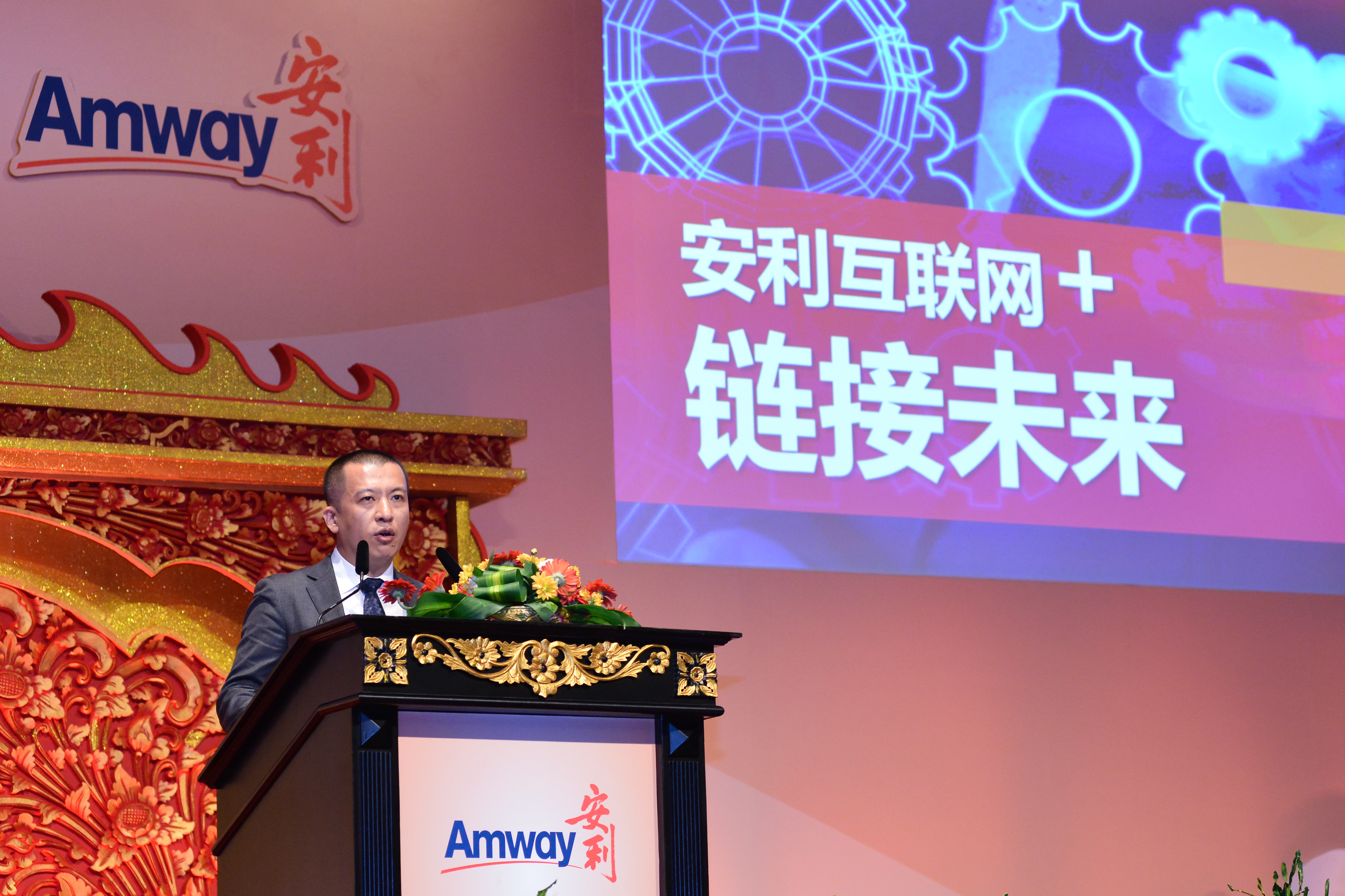活动现场，身着西装的发言者站在印有Amway、安利标识的精美雕花讲台后发言，背景大屏醒目展示“安利互联网+ 链接未来”字样，现场布置庄重正式，氛围专业积极，彰显安利探索数字化发展、布局未来的向好态势。