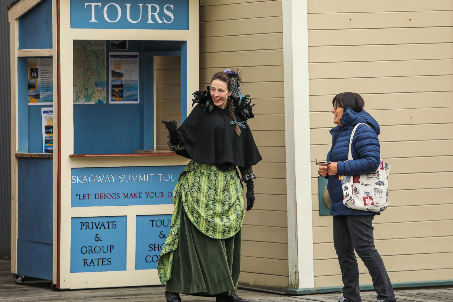 画面中是标有“TOURS”“SKAGWAY SUMMIT TOUR”“PRIVATE & GROUP RATES”字样的游览服务亭，身着复古服饰的导览人员正热情为安利出游伙伴介绍行程，现场氛围轻松融洽，尽显本次奖励旅程的丰富趣味。