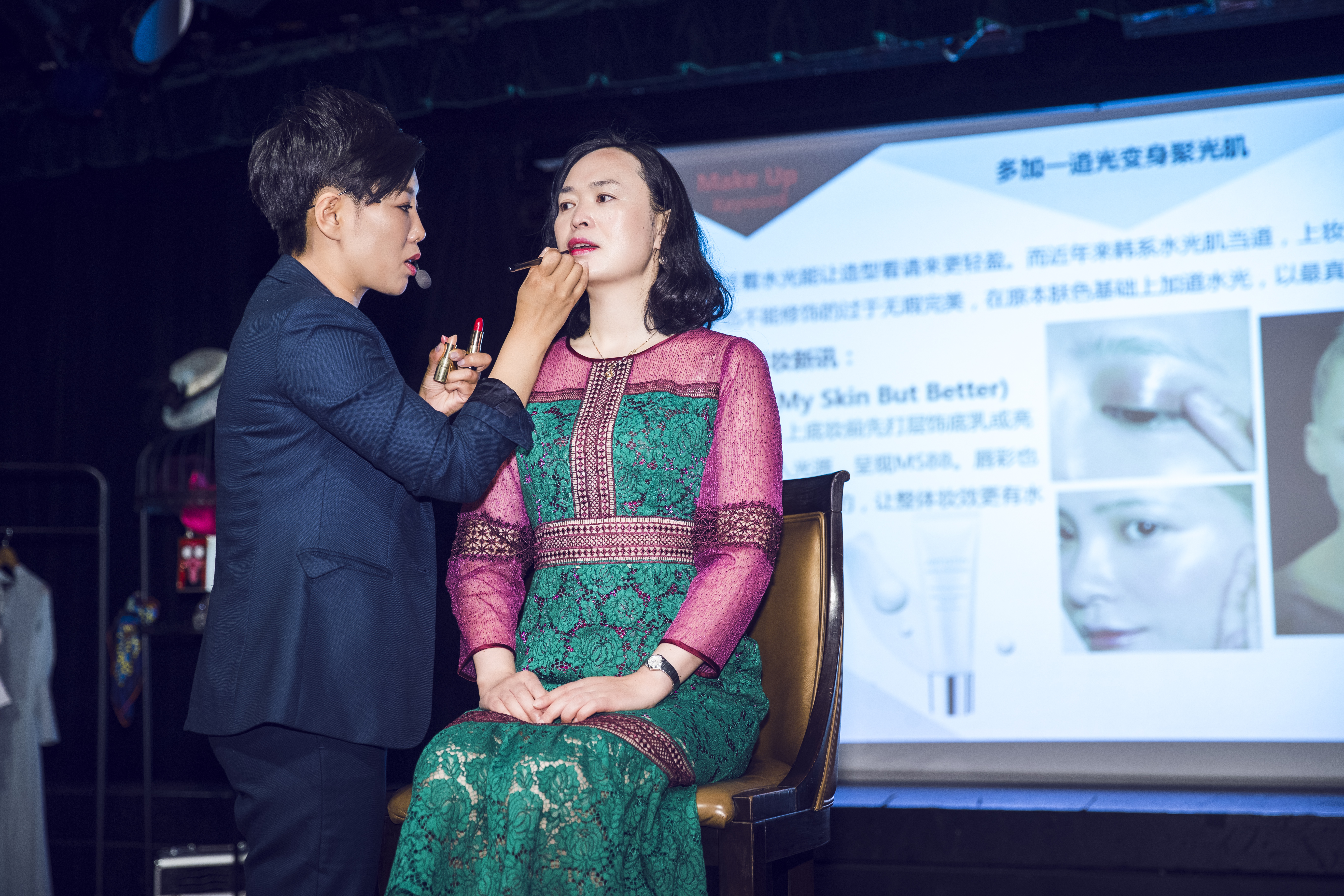 本次为安利美妆主题研讨活动现场，专业讲师正为到场嘉宾演示唇部妆容打造技巧，身后投影屏展示“多加一道光变身聚光肌”相关美妆教程内容，现场氛围专业实用，帮助参会伙伴掌握实用美妆技巧，感知安利美妆产品的优势。