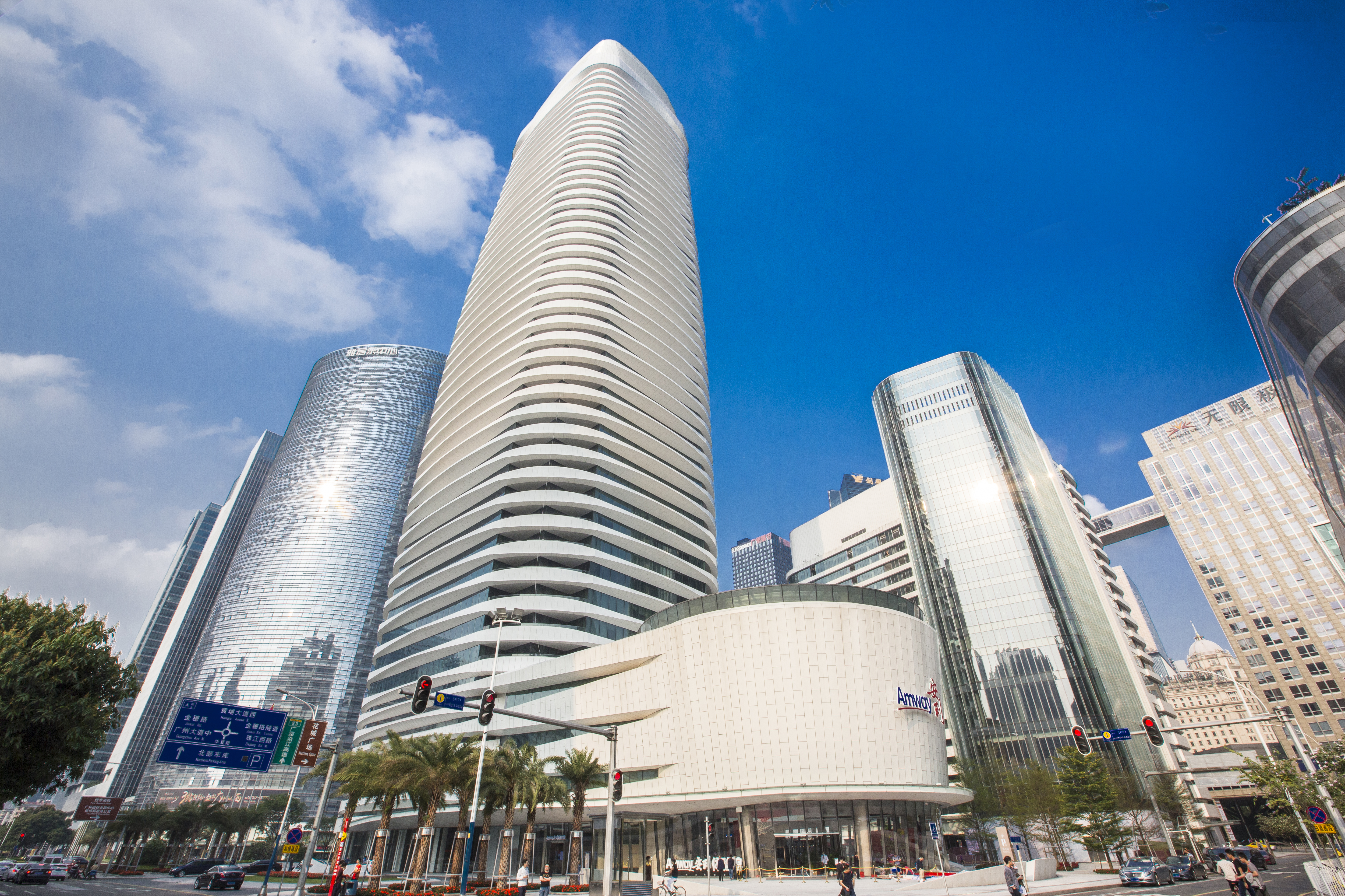 湛蓝晴空下，坐落于城市CBD的安利广州总部大厦外观现代大气，楼体底部设有清晰的“Amway”品牌标识，周边高楼林立、道路通畅，整体场景开阔明朗，尽显安利品牌的雄厚实力与高端质感。
