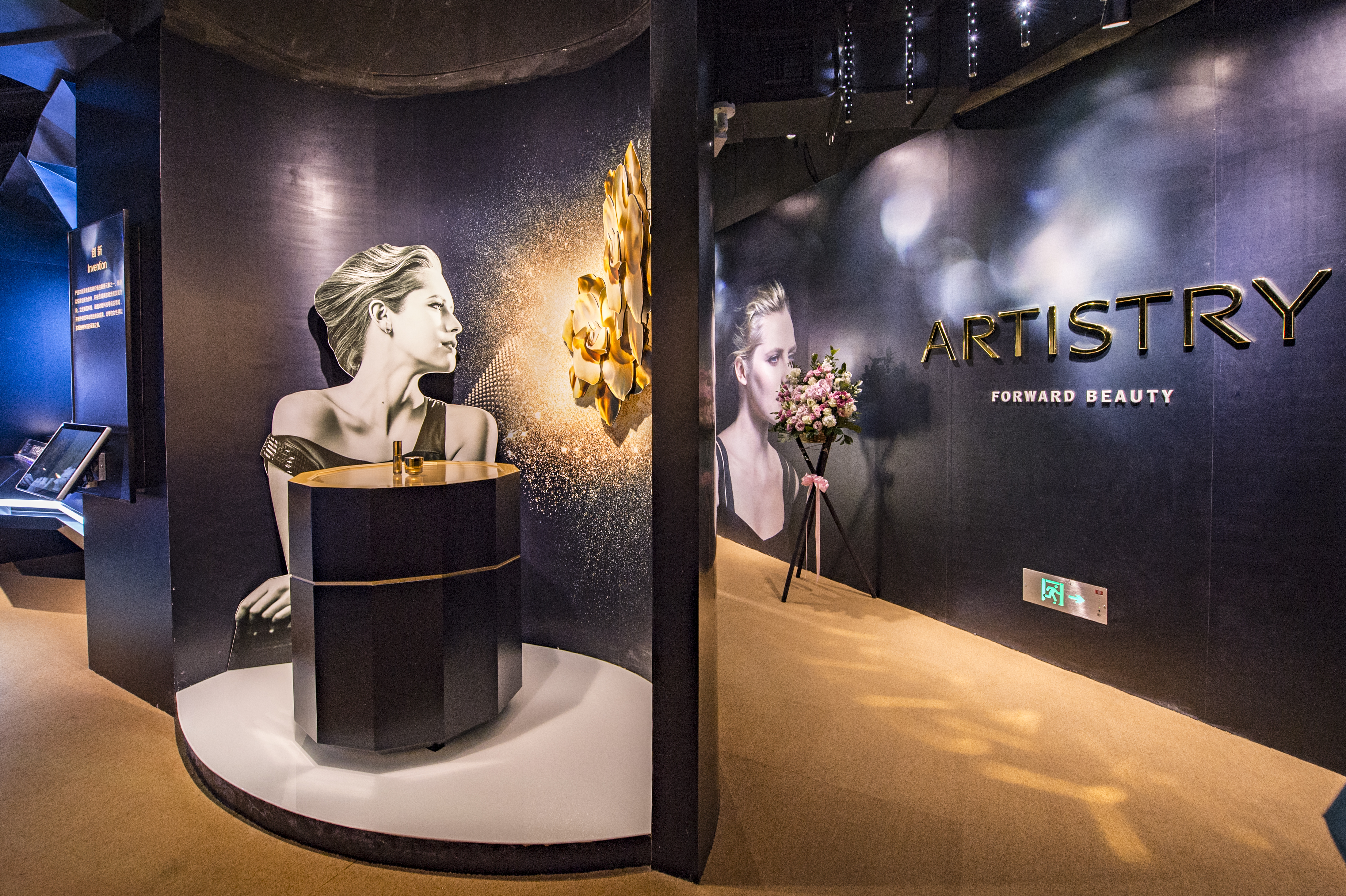 本区域为安利活动雅姿品牌展示专区，背景印有“ARTISTRY”“FORWARD BEAUTY”品牌字样，搭配质感品牌海报、产品展台与花艺装饰，整体设计高级精致，氛围轻奢大气，充分彰显雅姿高端美妆的品牌调性。