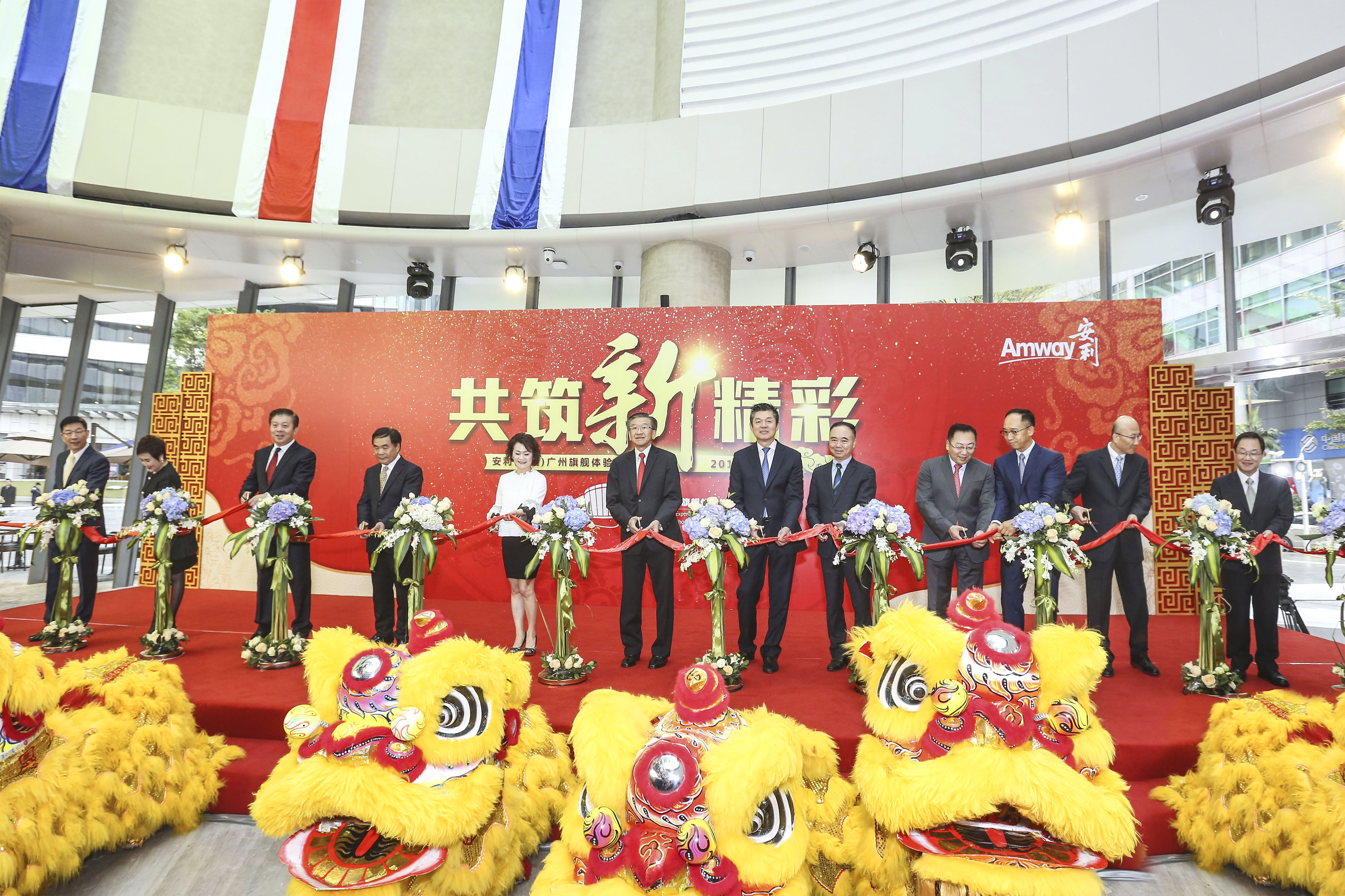 活动背景板印有“共筑新精彩”“Amway安利”“安利（中国）广州旗舰体验”字样，多位正装嘉宾立于红毯舞台共同持绸剪彩，台前摆放喜庆醒狮装饰，现场氛围隆重热烈，尽显开业活动的喜悦氛围与安利品牌的向好活力。