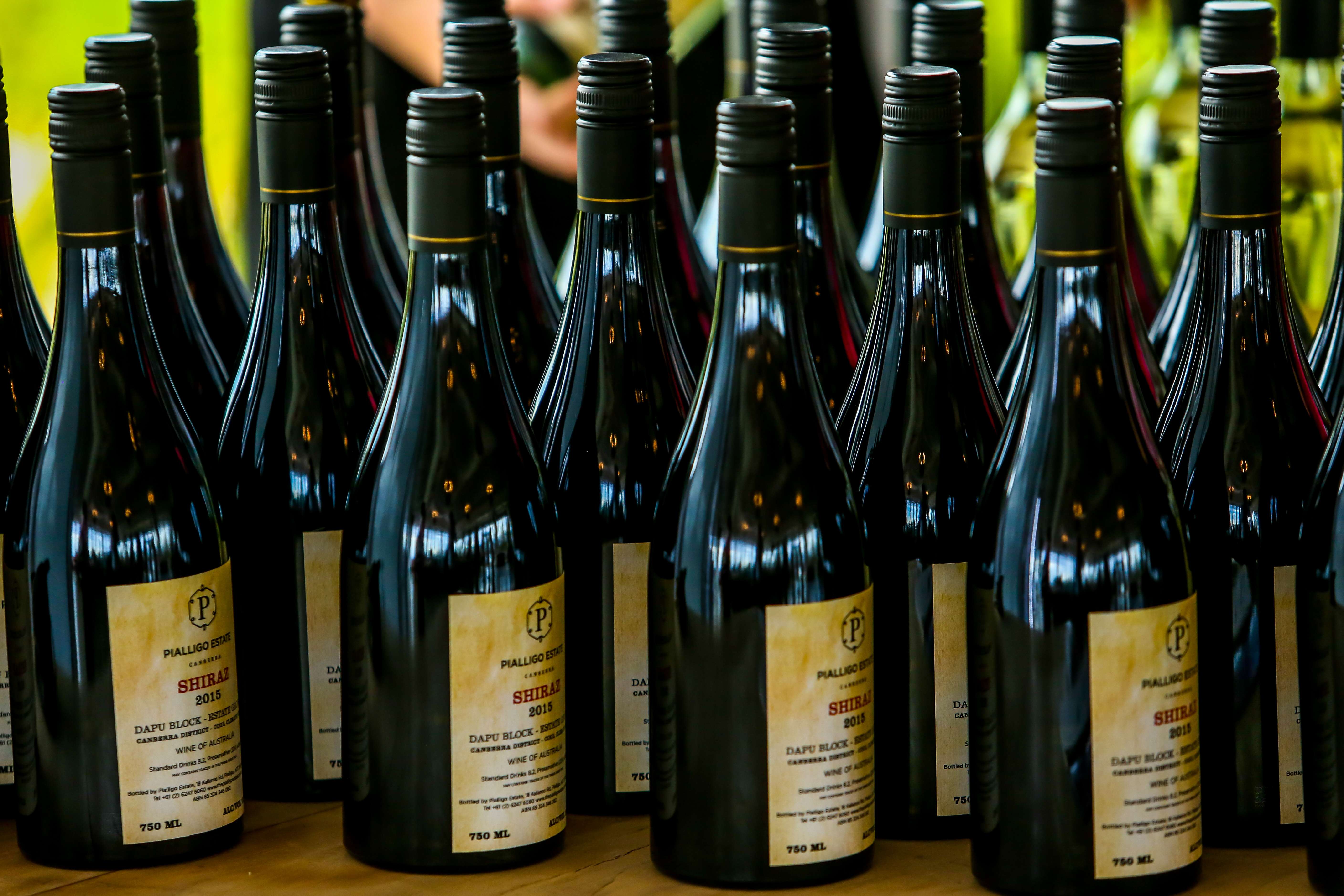 画面中多瓶澳大利亚产PIALLIGO ESTATE 2015年份SHIRAZ（西拉）红酒整齐排列，每瓶容量750ml，瓶身质感高级，排布规整有序，整体氛围精致高端，凸显安利活动的高规格与筹备用心，适配品鉴、伴手礼等场景。
