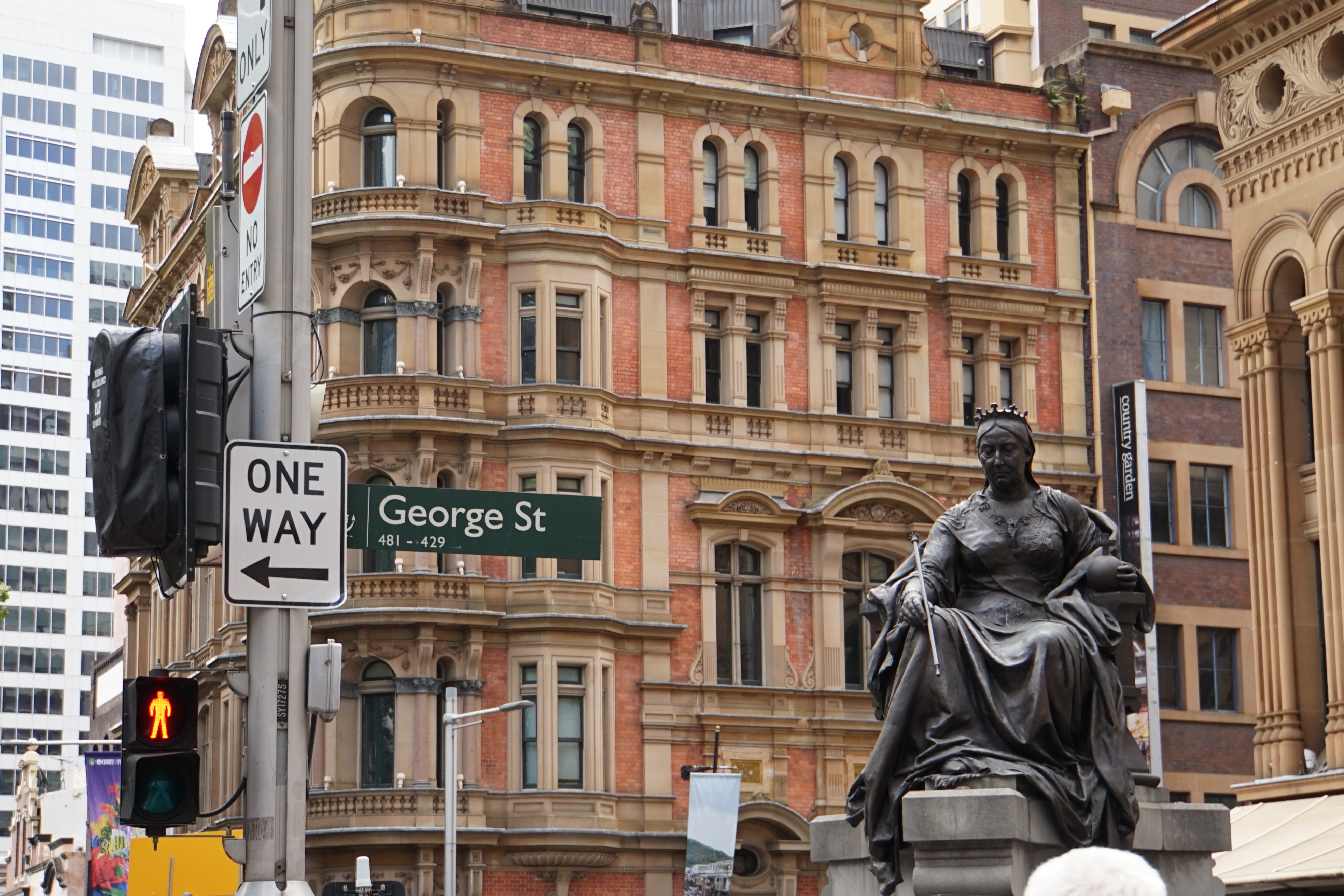 画面呈现安利海外活动探访的悉尼乔治街（George St）街景，右侧矗立维多利亚女王青铜雕像，背景是复古砖石结构的百年历史建筑，路旁设置ONE WAY单行、NO ENTRY禁入等交通标识，街区异域风情浓郁，氛围厚重雅致。