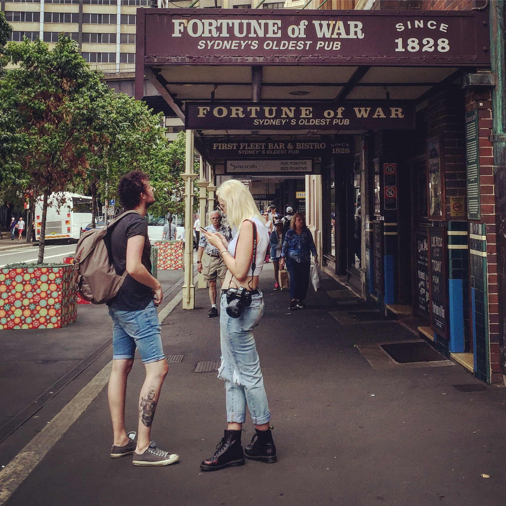 画面取景于悉尼始建于1828年的老牌酒馆FORTUNE of WAR门前，参与安利海外游学的伙伴在此停留，周边街道整洁、绿植繁茂，来往行人络绎，整体氛围轻松愉悦，充分展现出安利游学行程的丰富体验感。