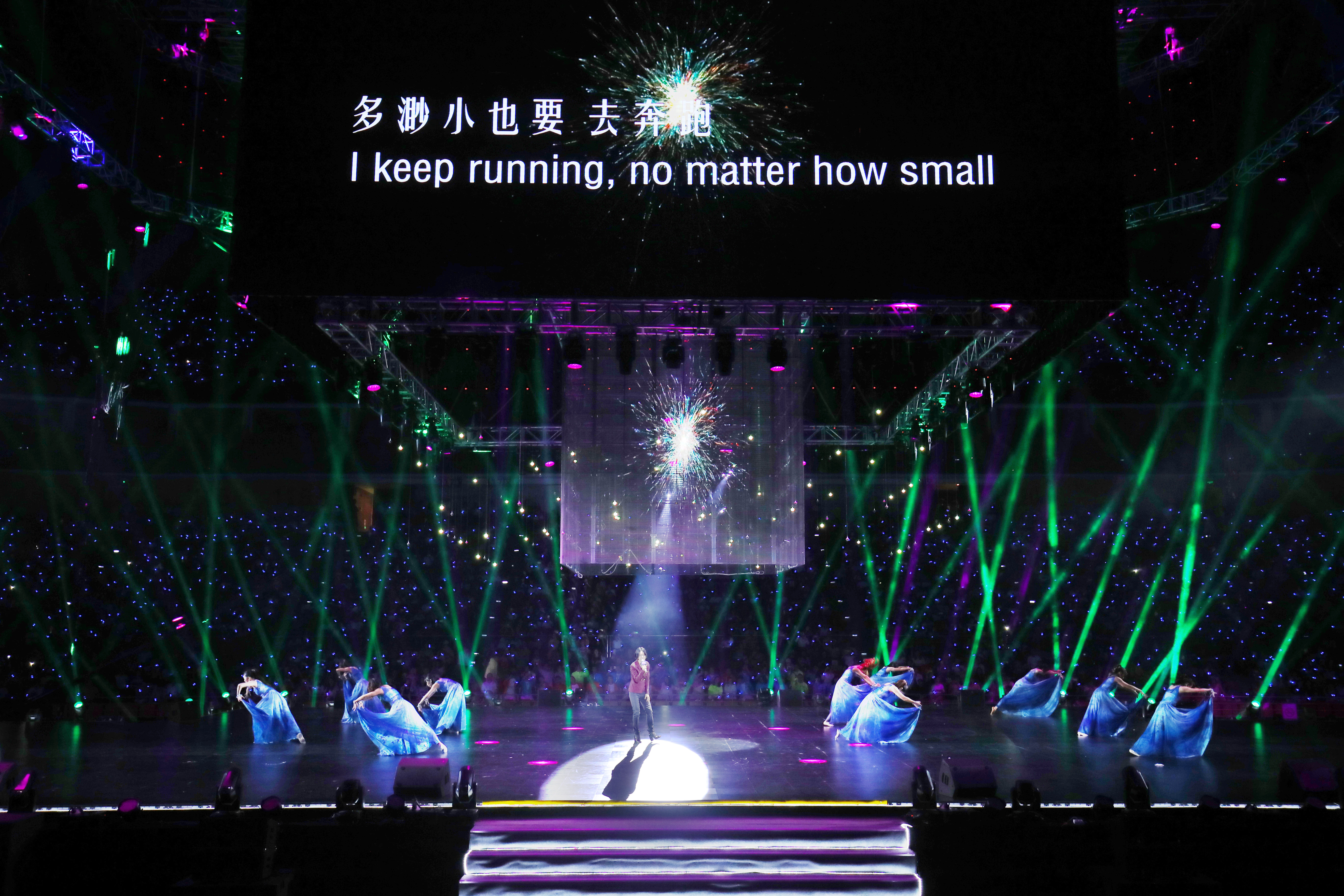 本次安利年会演出现场，背景屏展示着励志标语“多渺小也要去奔跑 I keep running, no matter how small”，舞台中央歌手倾情献唱，身着蓝色长裙的舞者配合伴舞，炫目的灯光交错辉映，台下观众座无虚席，现场氛围昂扬热血，传递出奋进向上的品牌精神。