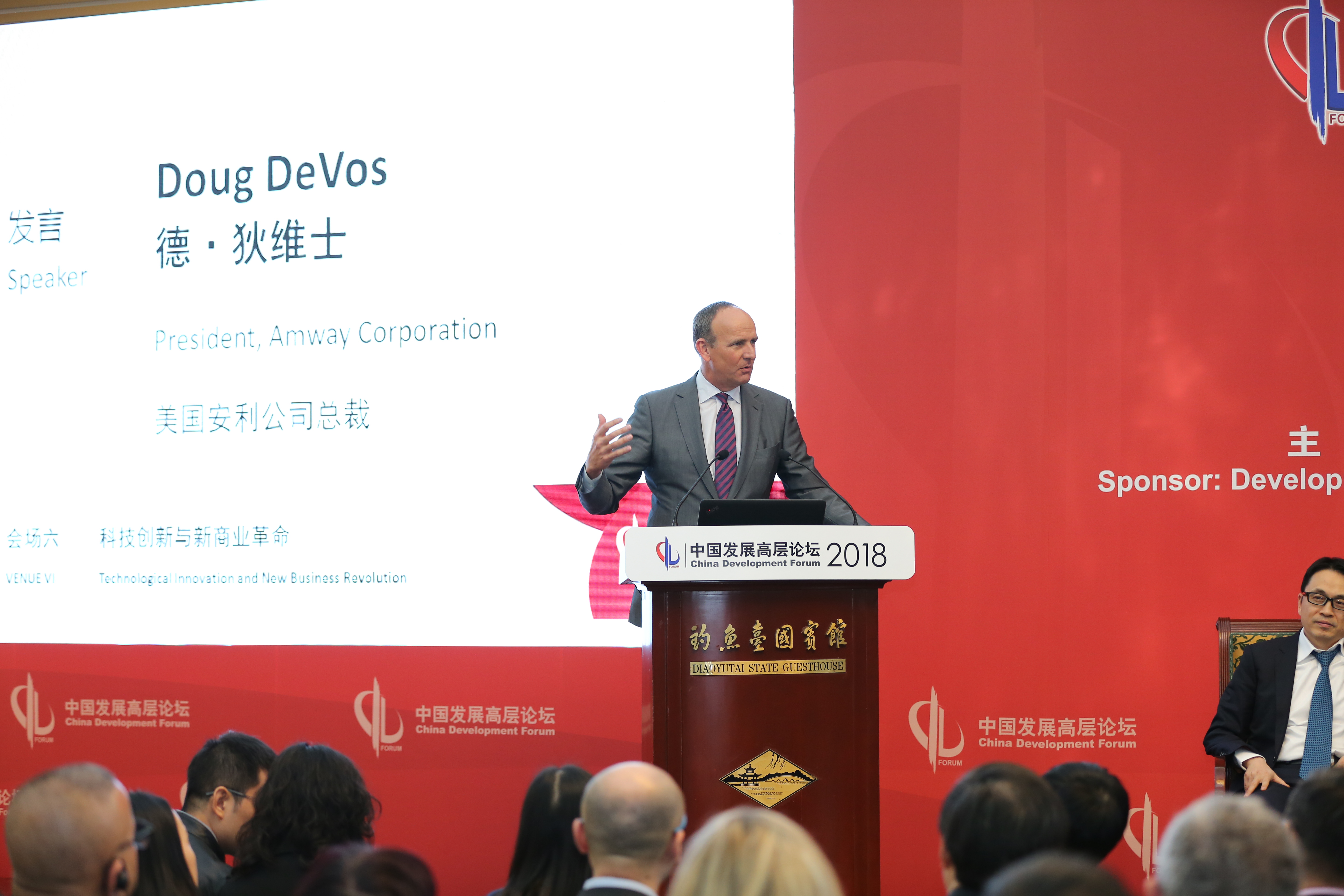 2018中国发展高层论坛于钓鱼台国宾馆举办，本次会场主题为“科技创新与新商业革命”，美国安利公司总裁德·狄维士作为发言嘉宾登台演讲，他神态从容、手势自然，台下参会嘉宾专注聆听，现场氛围庄重专业，展现安利深度参与行业前沿交流的积极姿态。