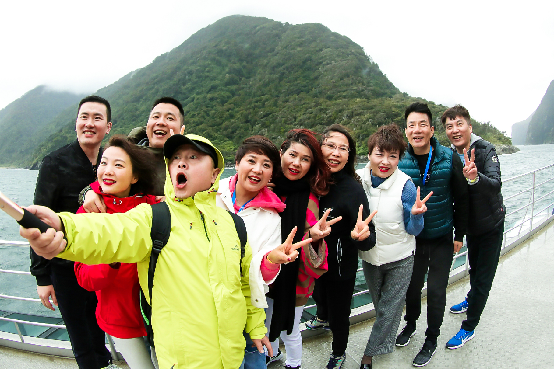 安利团建活动中，多位伙伴相聚于峡湾游船上，背靠覆满绿植的青山与开阔水域，大家笑容明媚神采飞扬，有人举着自拍杆记录欢聚时刻，不少人比出剪刀手，氛围轻松欢快，充分展现出安利团队融洽的凝聚力与蓬勃活力。