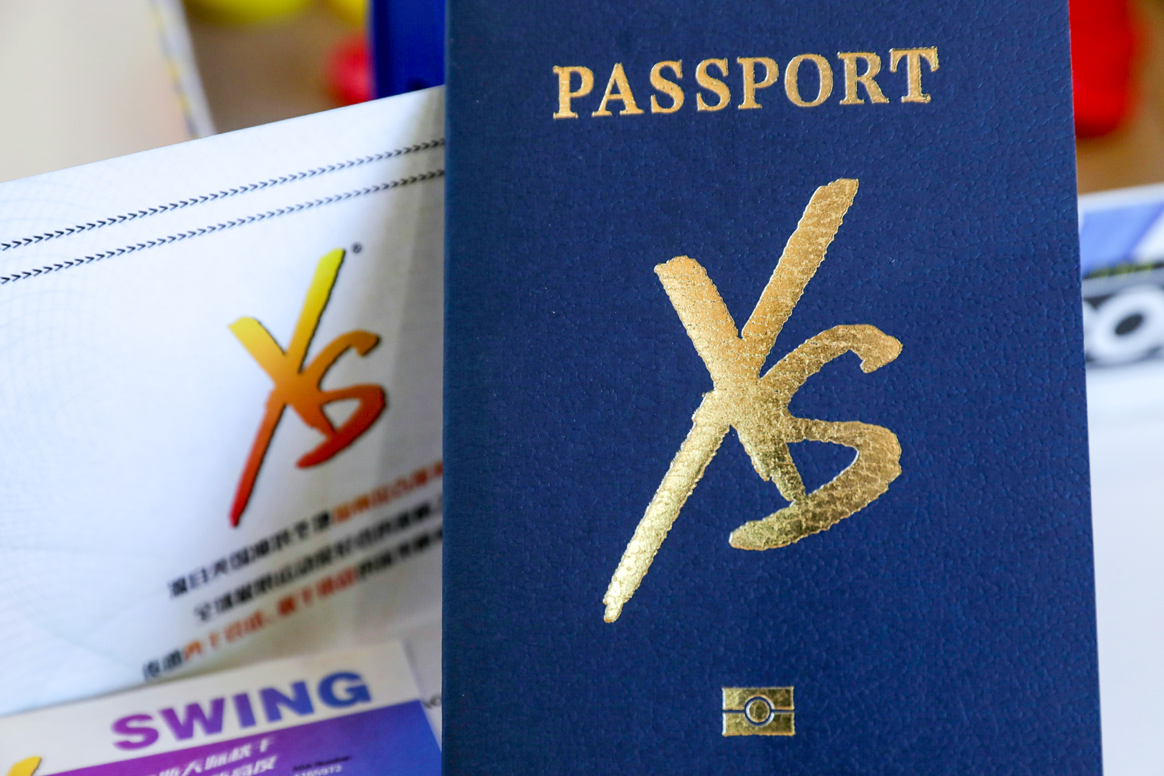 画面主体是藏蓝色质感封皮的安利XS专属护照，封皮烫金印有“PASSPORT”字样与XS品牌标识，精致高级。旁侧摆放印有XS标识、“SWING”字样的品牌宣传物料，整体仪式感十足，凸显XS活动专属属性与品牌活力调性。