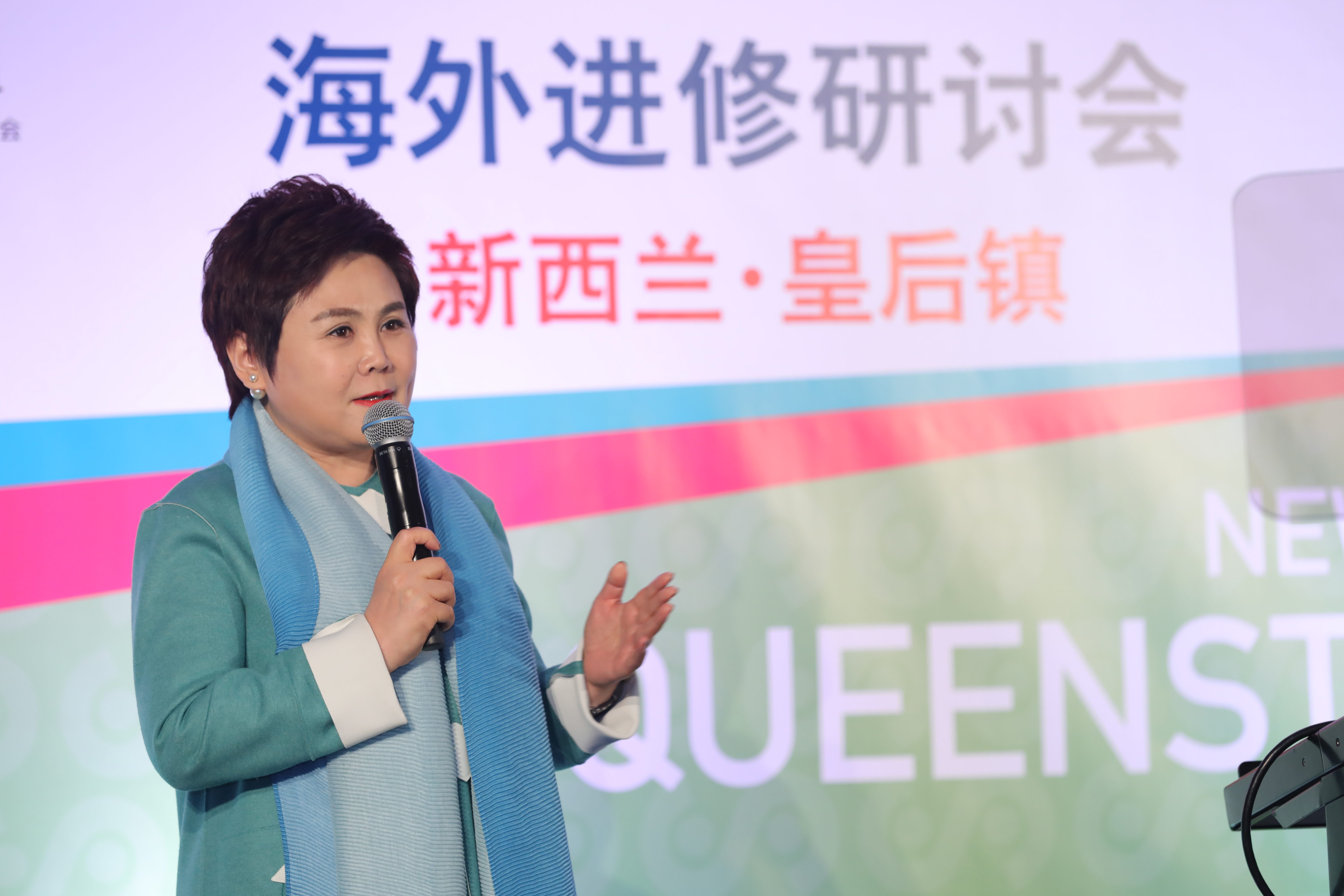 本次是安利新西兰·皇后镇海外进修研讨会活动现场，主讲嘉宾手持麦克风正进行分享，姿态从容专业，输出优质成长内容，现场氛围积极向上，充分展现出安利研修活动的专业属性与奋进的品牌风貌。