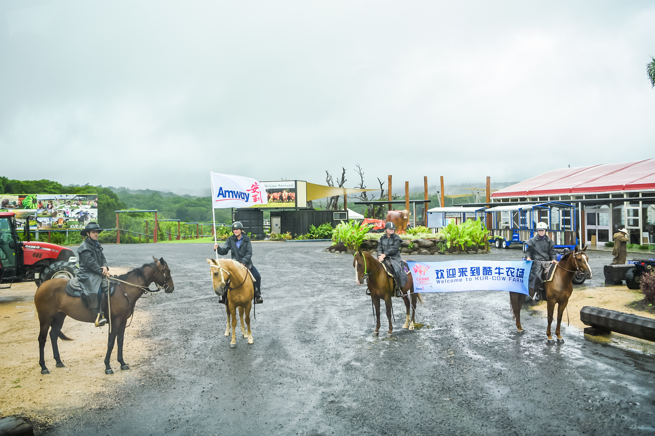 画面为酷牛农场活动现场，四位骑手骑马列队，一人高举印有“Amway安利”字样的品牌旗帜，另外两人拉着印有“欢迎来到酷牛农场Welcome to KUR-COW FARM”的横幅，以特色仪式欢迎到访的安利活动参与者，现场氛围郑重热情，尽显活动的创意与活力。