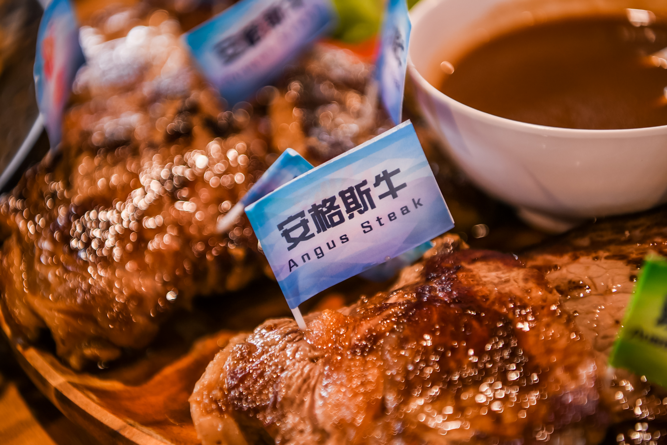 本图为安利品牌活动餐区的餐食展示，油润亮泽的煎制安格斯牛排上插有标注“安格斯牛 Angus Steak”的标识牌，旁侧配有佐餐酱汁，餐食精致诱人，尽显活动筹备的贴心细致，为参会伙伴带来高品质用餐体验。