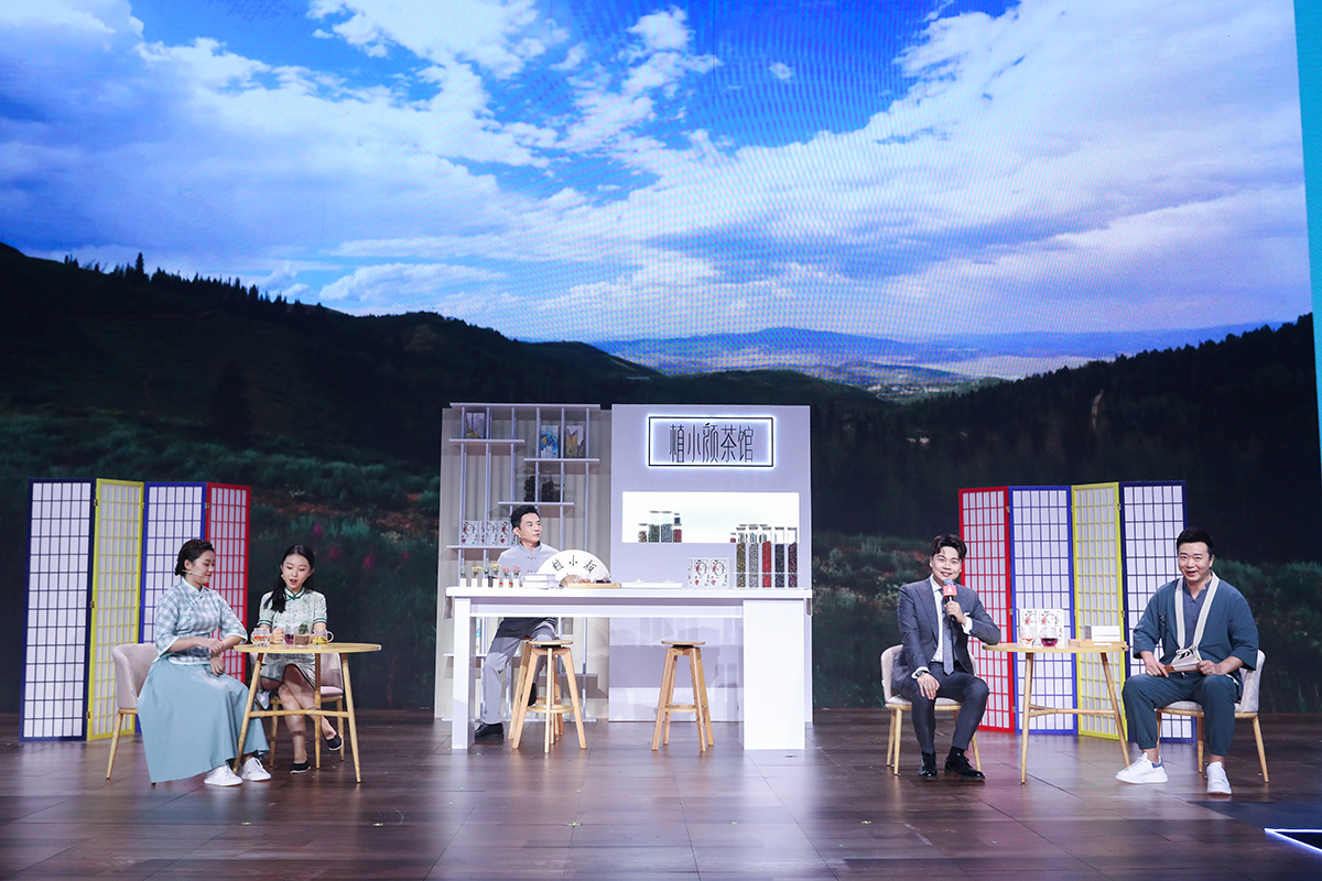 活动舞台以山林蓝天景观为背景，中央搭建“植小颜茶馆”主题展区，搭配国风屏风、茶桌陈设，多位嘉宾围坐互动，主持人手持话筒交流分享，整体氛围轻松鲜活，充分传递安利植小颜的国风健康品牌特质。