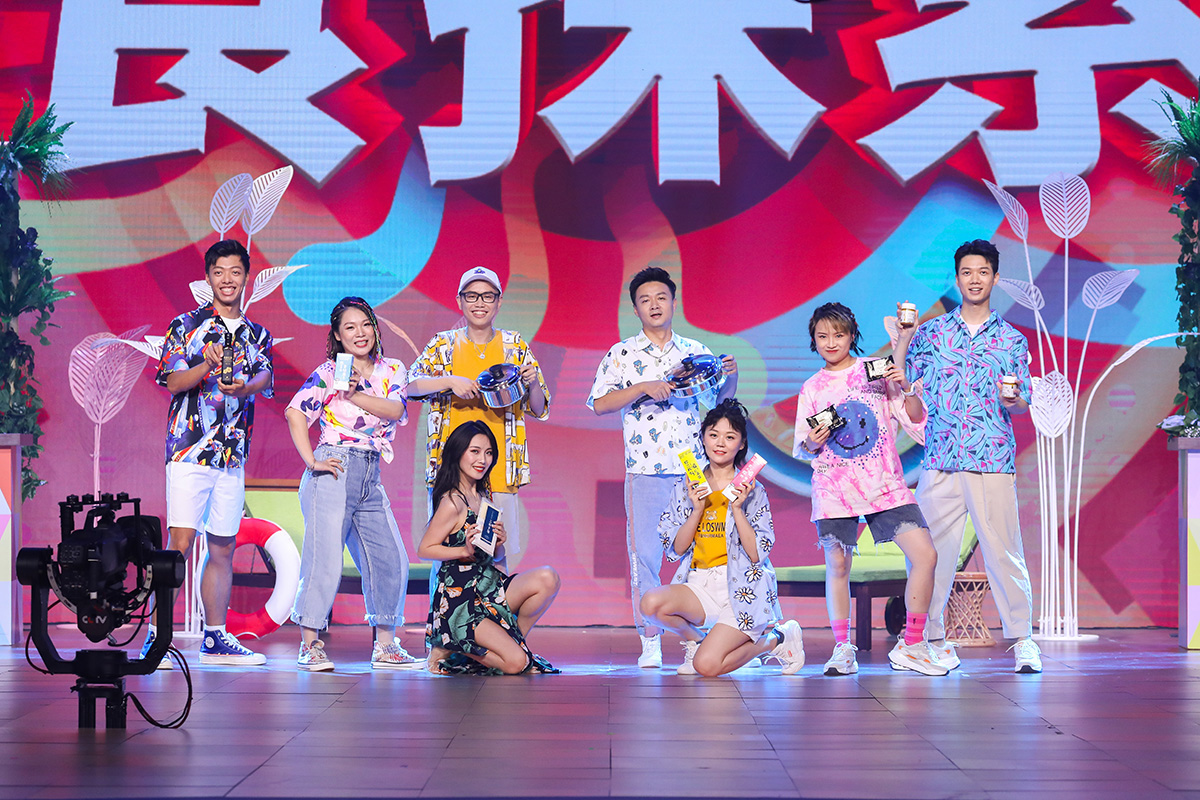 本次安利品牌活动现场，色彩明快的舞台背景醒目呈现“快乐”主题字样，多位身着休闲活力着装的伙伴在台上前蹲后站合影，众人手持安利旗下多元产品及家居好物，笑容灿烂，现场氛围轻松欢快，尽显品牌年轻活力的风貌与积极欢乐的活动氛围。