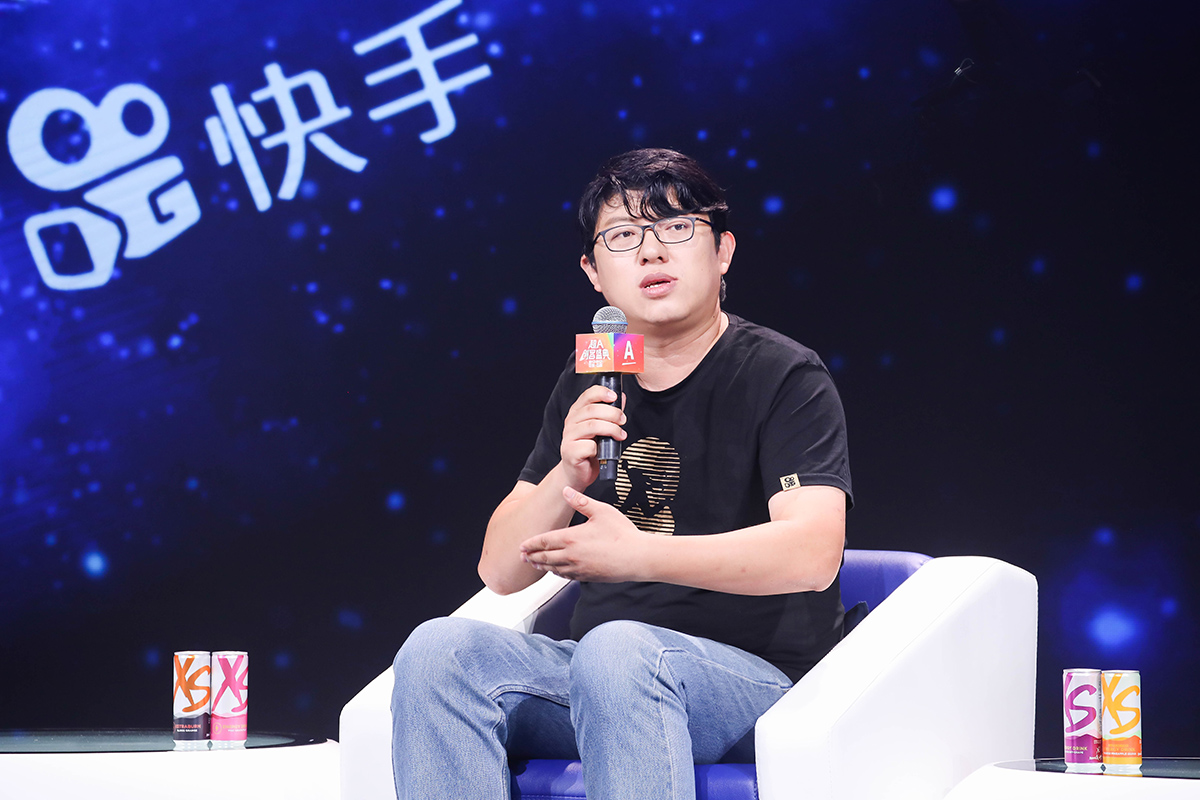 活动现场背景带有快手标识，男性嘉宾手持印有“创客盛典”字样的麦克风正在交流发言，现场摆放安利XS系列饮品，整体氛围专业活跃，充分展现出本次创客交流活动的正向活力。