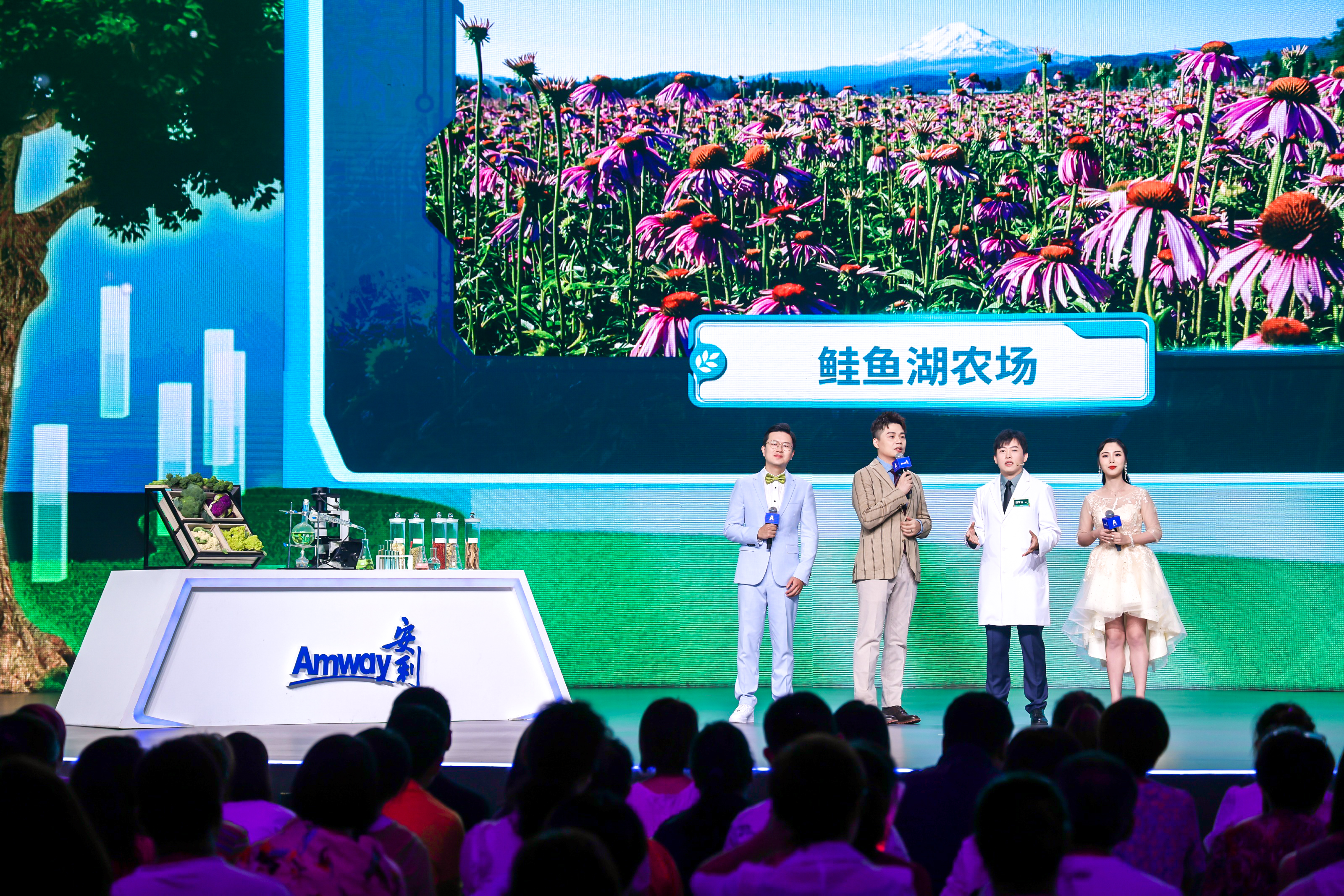 活动现场背景大屏展示着标注“鲑鱼湖农场”的种植景观，四位嘉宾站在印有“Amway 安利”标识的舞台上做分享，舞台侧方展示台摆放着植物原料、实验器具，台下坐满观众，现场氛围专业鲜活，充分展现安利对原料品质的严格把控。