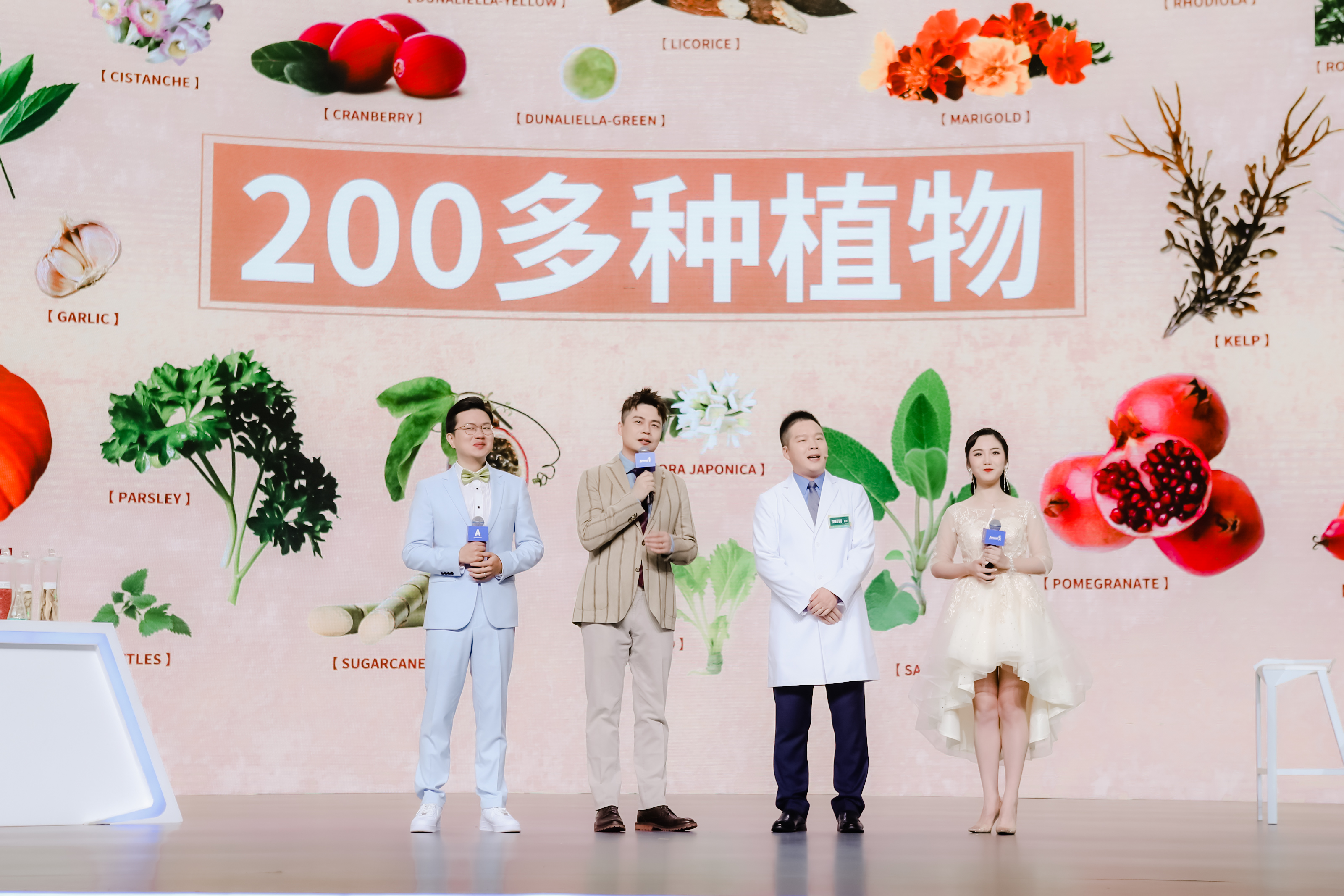 活动现场背景醒目标注“200多种植物”字样，搭配蔓越莓、石榴、甘草等多种植萃原料图示，主持人与研发专家等四位嘉宾站在舞台上手持话筒开展科普分享，氛围专业生动，展现安利在植物营养领域的研发优势。