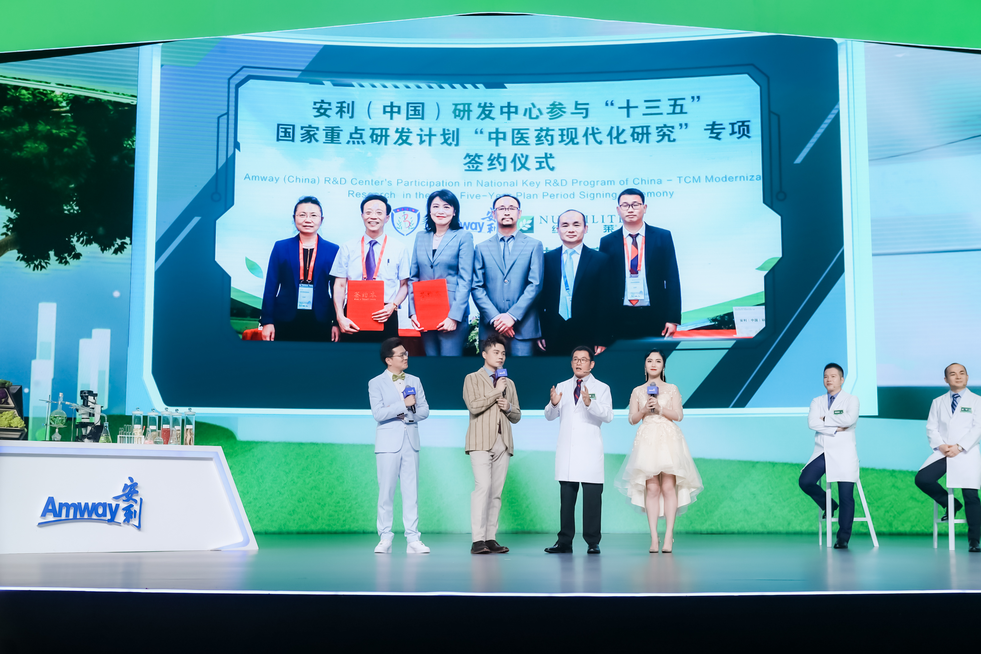 活动现场背景大屏展示安利（中国）研发中心参与“十三五”国家重点研发计划“中医药现代化研究”专项签约仪式相关内容，舞台上主持人与研发专家正在互动分享，现场氛围专业正式，充分展现安利在大健康科研领域的投入与实力。