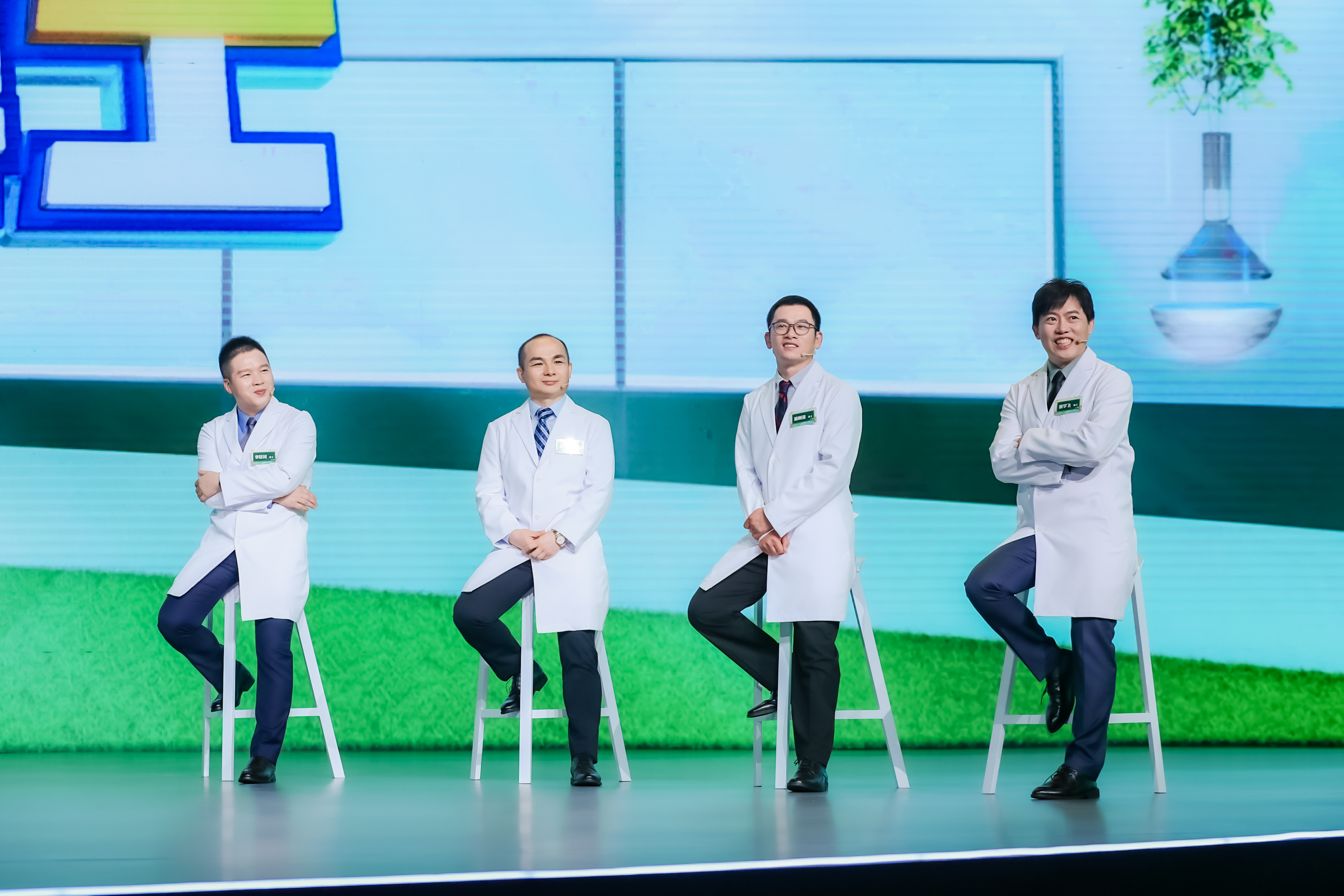 活动舞台上，四位身着白大褂的安利科研专家坐于白色高脚凳上，状态昂扬、专业从容，背景是清新科技风的活动大屏，氛围积极正向，充分展现安利研发团队的硬核实力，传递品牌对产品品质与研发的高度重视。