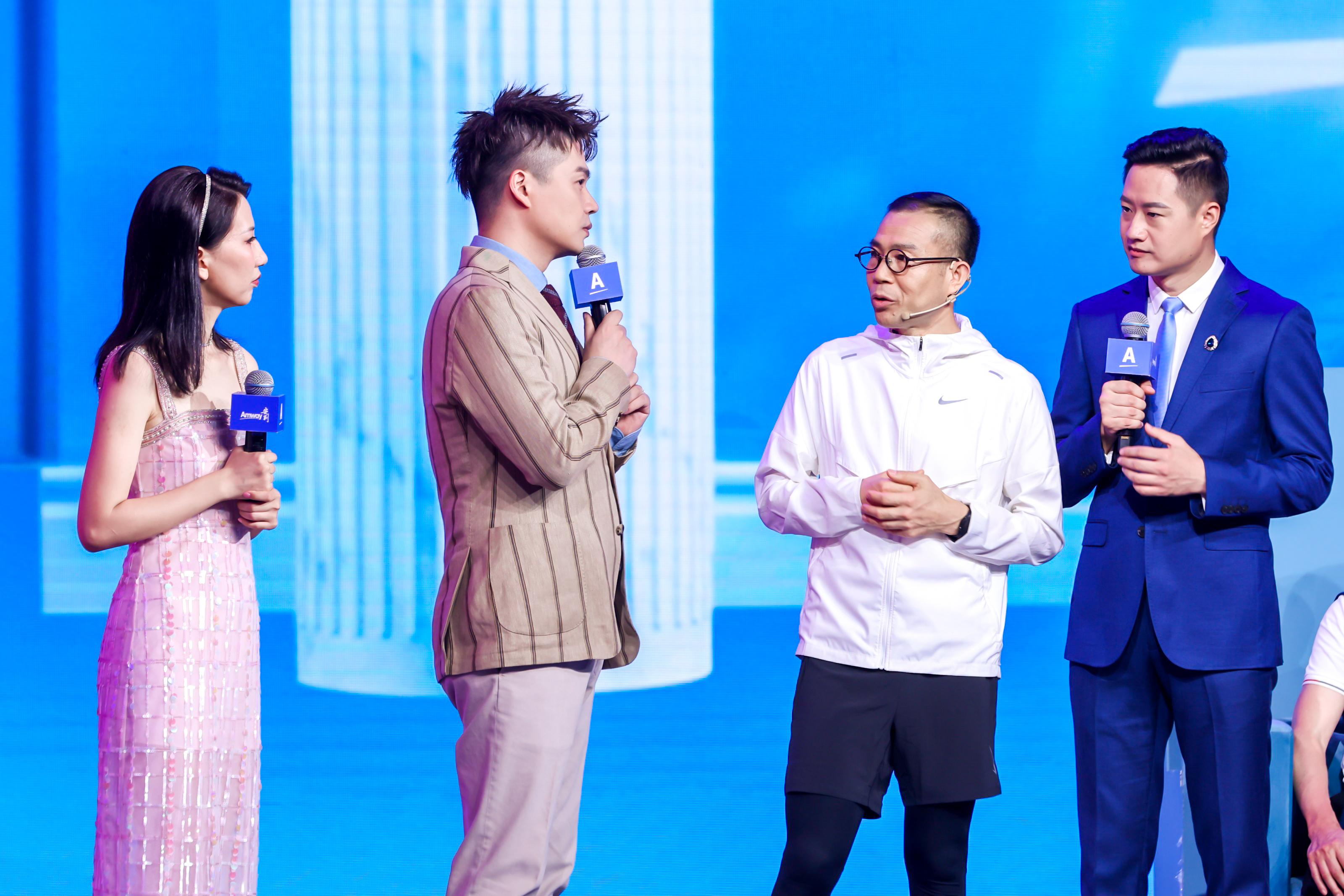 本次安利品牌活动现场，蓝色背景清爽明快，两名主持人手持印有“Amway”“A”标识的专属话筒，与两位受邀嘉宾现场对谈交流，氛围专业活跃，充分展现出活动开放沟通、共探发展的积极特质。