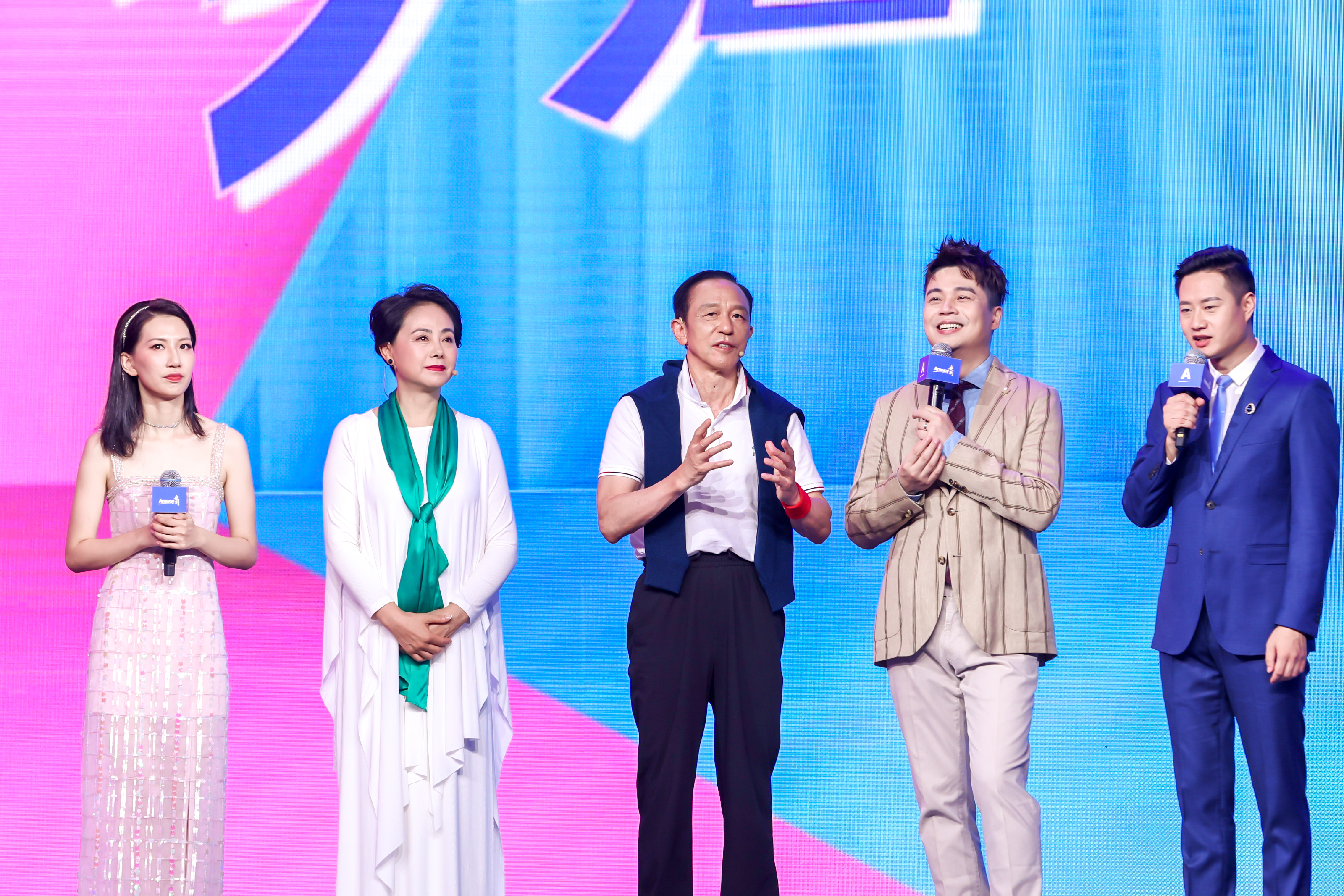 本次安利品牌活动现场，五位嘉宾立于粉蓝渐变的主题舞台之上，手持印有安利标识的话筒，中间嘉宾正侃侃而谈分享感悟，其余嘉宾或认真倾听或含笑以待，现场氛围热烈正向，尽显安利活动的昂扬活力与积极风貌。