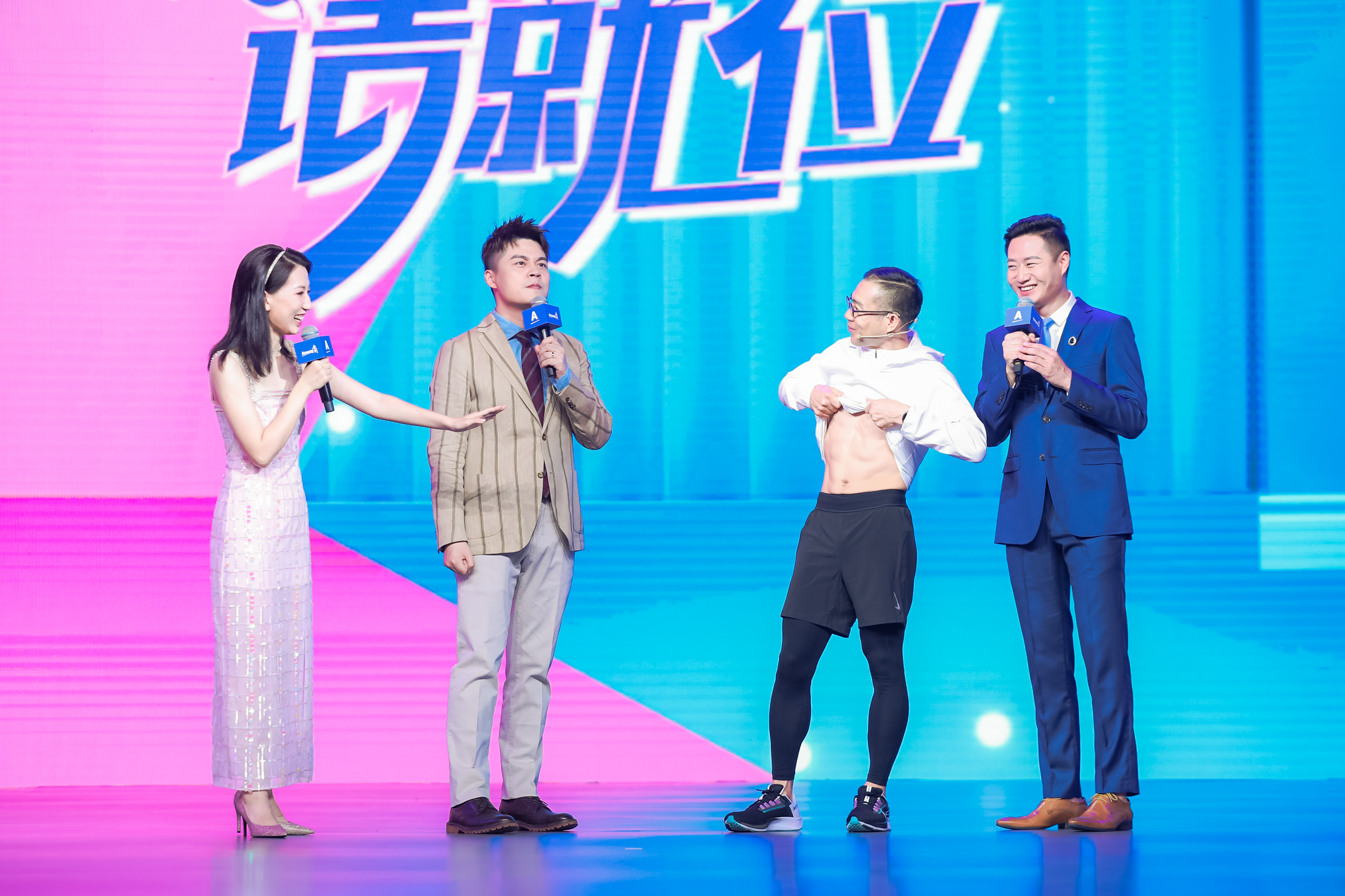 活动舞台背景带有“请就位”字样，粉蓝渐变底色明快活泼。现场一位身着运动装的嘉宾展示健身成果，三位主持人手持印有安利标识的话筒与之友好互动，现场氛围轻松热烈，充分传递出安利倡导健康美好生活的品牌理念。