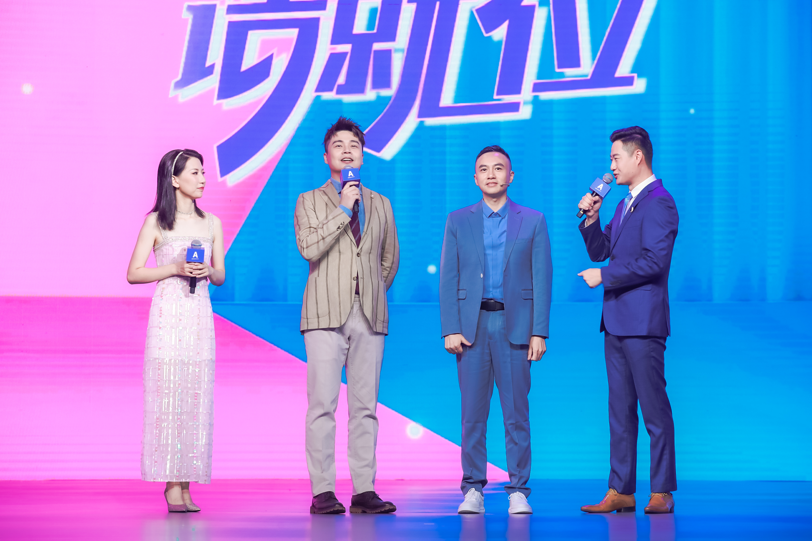 本次安利品牌活动现场，粉蓝渐变的主舞台明亮鲜活，四位主持人与嘉宾手持印有安利品牌标识的麦克风互动交流，背景醒目呈现“绮就位”字样，现场氛围轻松热烈，尽显活动积极向上的昂扬风貌。