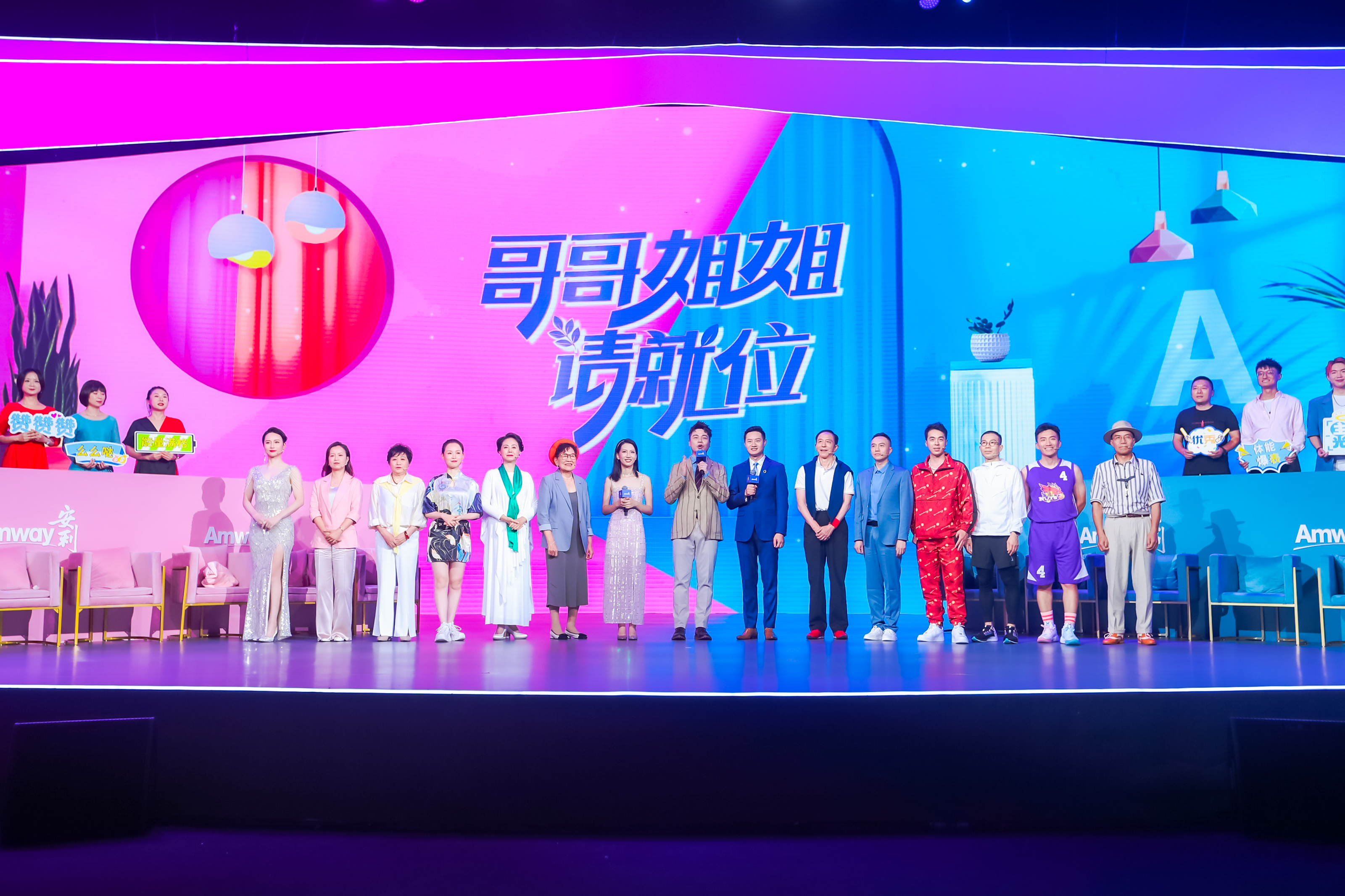 本次为安利品牌活动现场，背景大屏醒目显示核心字样“哥哥姐姐请就位”，十余位不同年龄段、风格各异的嘉宾整齐站立在绚丽舞台上，现场氛围明快活力，充分彰显安利活动积极多元、充满生命力的品牌特质。