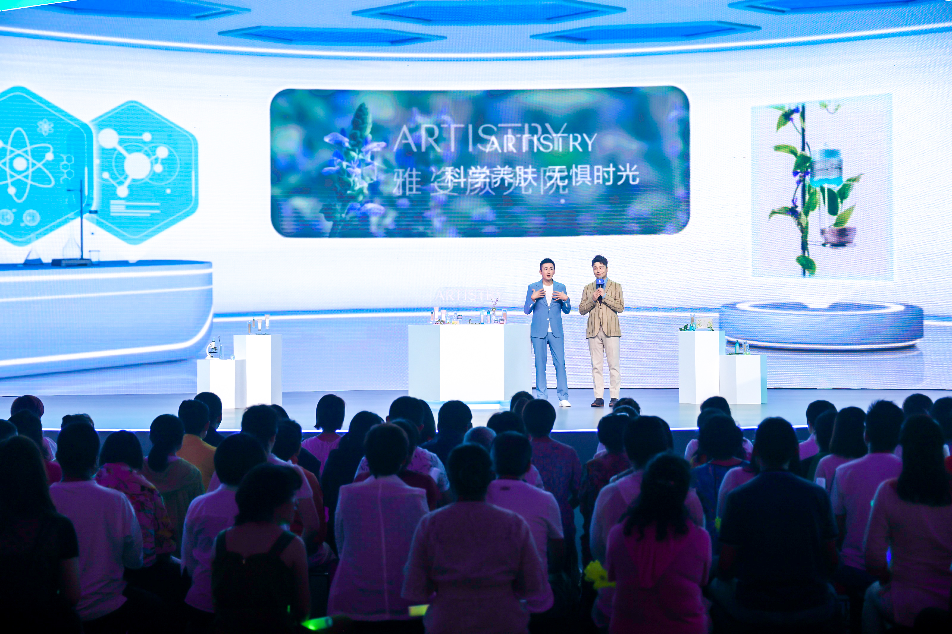 活动现场背景大屏展示“ARTISTRY雅姿 科学养肤无惧时光”品牌标语，两位嘉宾站在陈列雅姿产品的舞台上开展分享，台下坐满认真聆听的参会人员，整体氛围专业热烈，充分展现雅姿科技护肤的品牌优势。