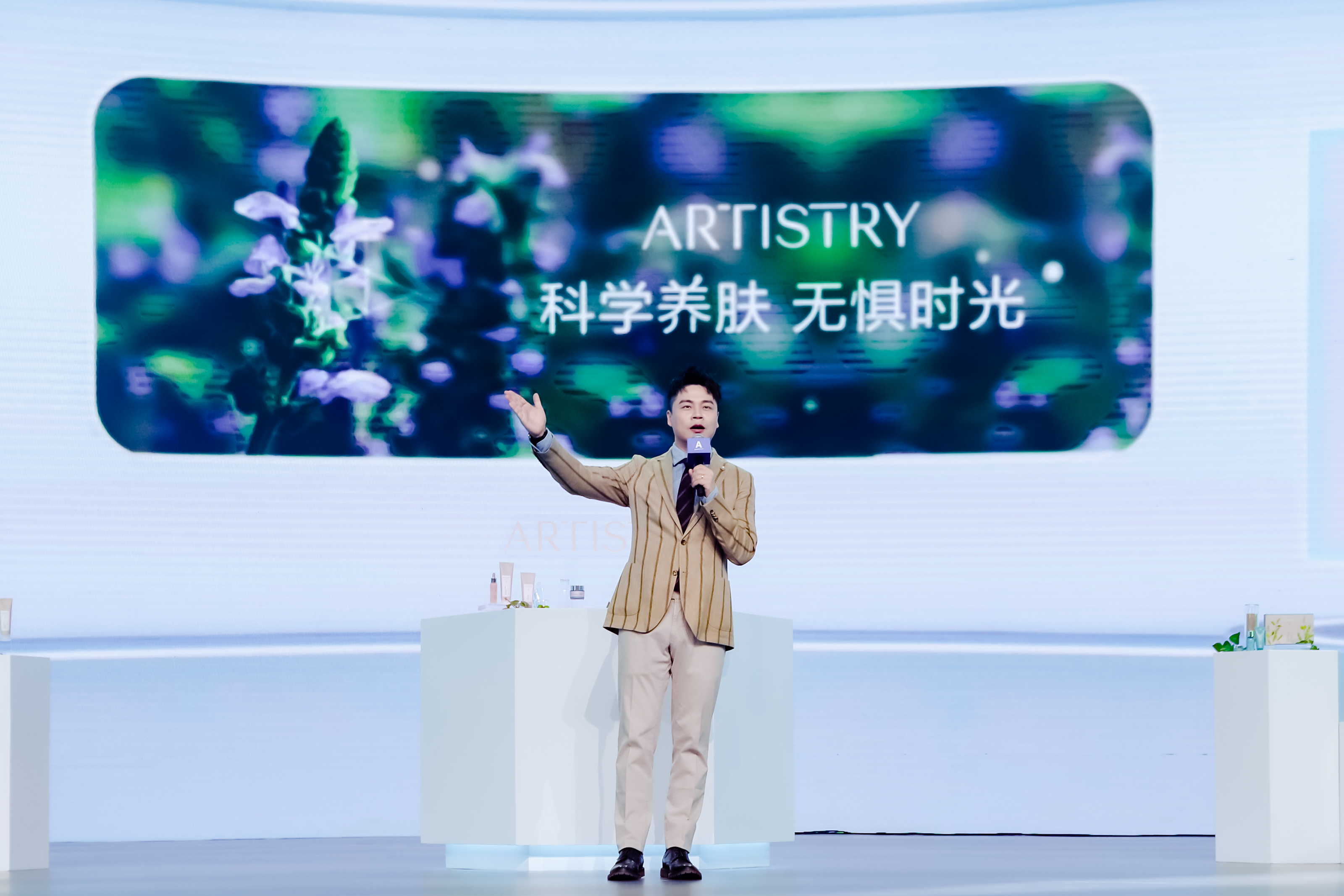 活动现场，主讲嘉宾手持话筒站在舞台上做内容分享，身后大屏醒目呈现“ARTISTRY 科学养肤 无惧时光”的主题字样，台前展台上陈列着雅姿相关护肤产品，整体氛围专业明快，传递出雅姿专业护肤的品牌理念。