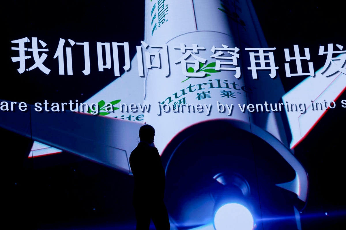活动现场大屏展示“我们叩问苍穹再出发”主题标语，搭配印有纽崔莱（nutrilite）标识的火箭视觉元素，演讲者剪影伫立台前，整体氛围昂扬壮阔，充分传递出安利迈向全新发展阶段的信心与决心。