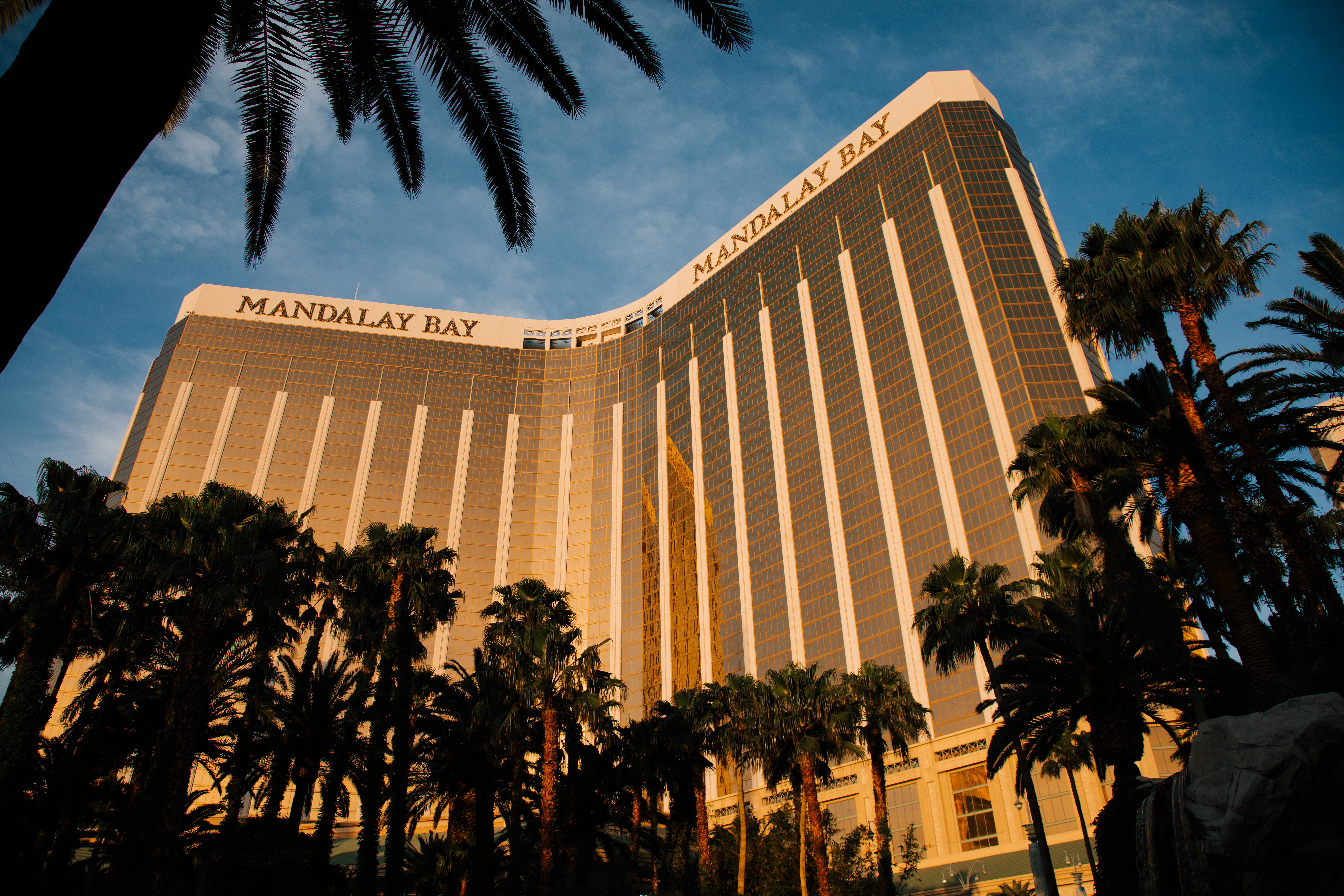 画面展现晴朗晴空下的曼德勒海湾（MANDALAY BAY）酒店，建筑外立面为鎏金玻璃材质，造型恢弘大气，周边环绕着葱郁棕榈树，整体氛围开阔明亮，作为安利海外品牌活动举办场地，尽显高端气派的活动格调。
